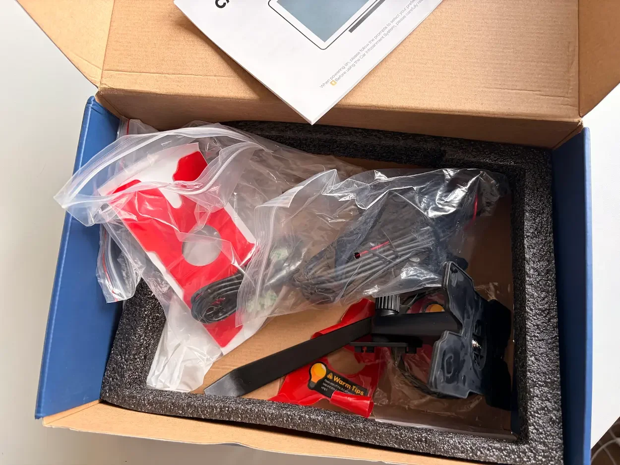 Open LAMTTO CarPlay screen box containing the mounting brackets, cables, reversing camera accessories and instruction leaflet.