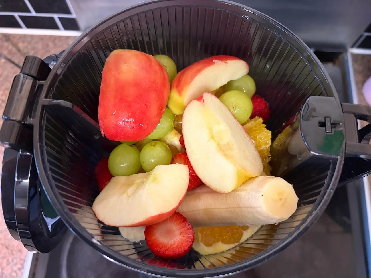 Sliced red apples, green grapes, strawberries and banana loaded into the AMZCHEF cold press juicer.