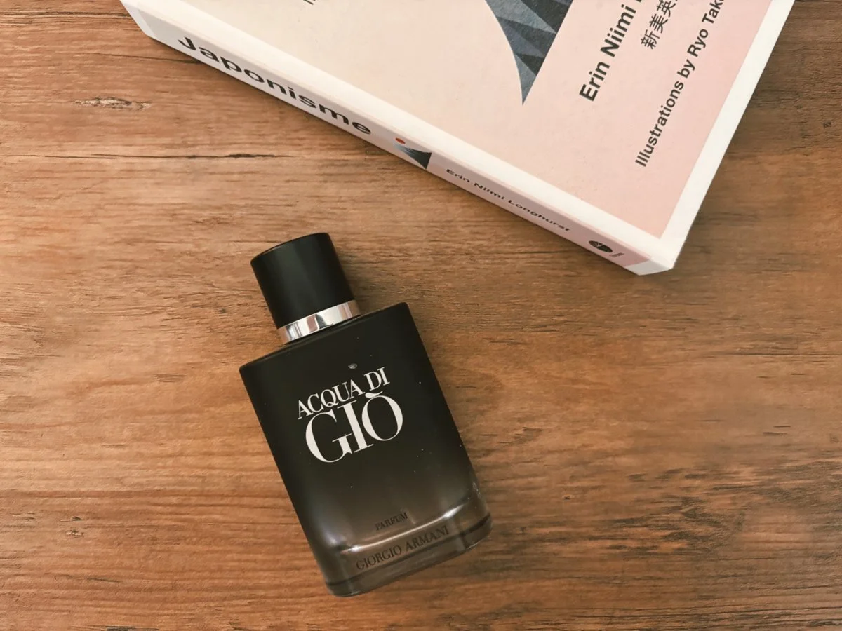 Acqua Di Gio Parfum by Giorgio Armani bottle on wooden surface near lifestyle books