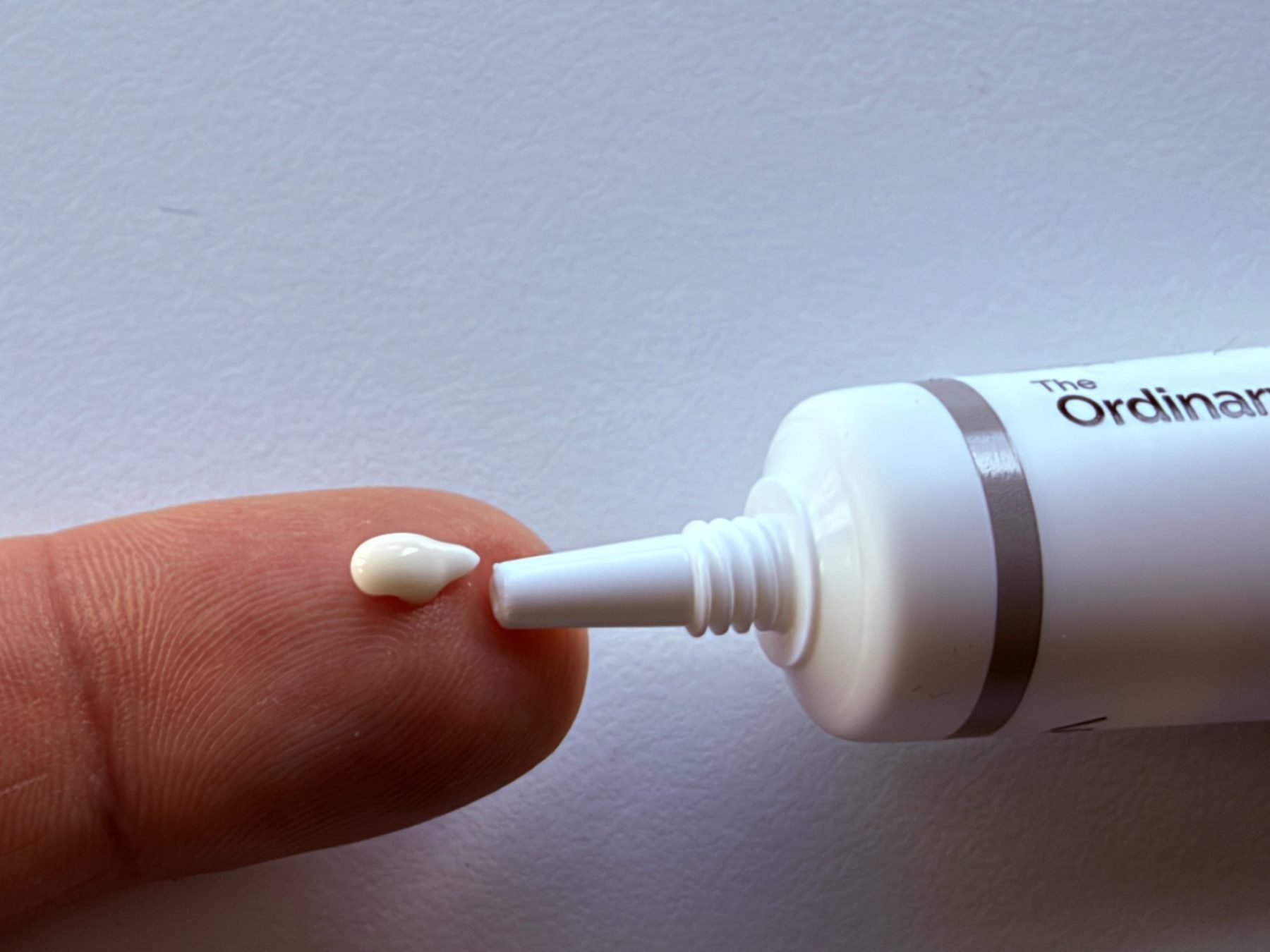 A small amount of The Ordinary Lacto-PDRN 4% + B9 Eye Cream on a fingertip beside the open tube.