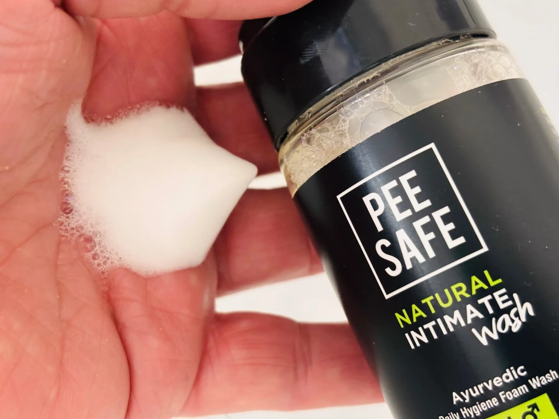 Pee Safe Natural Intimate Wash foam shown in hand beside the bottle.