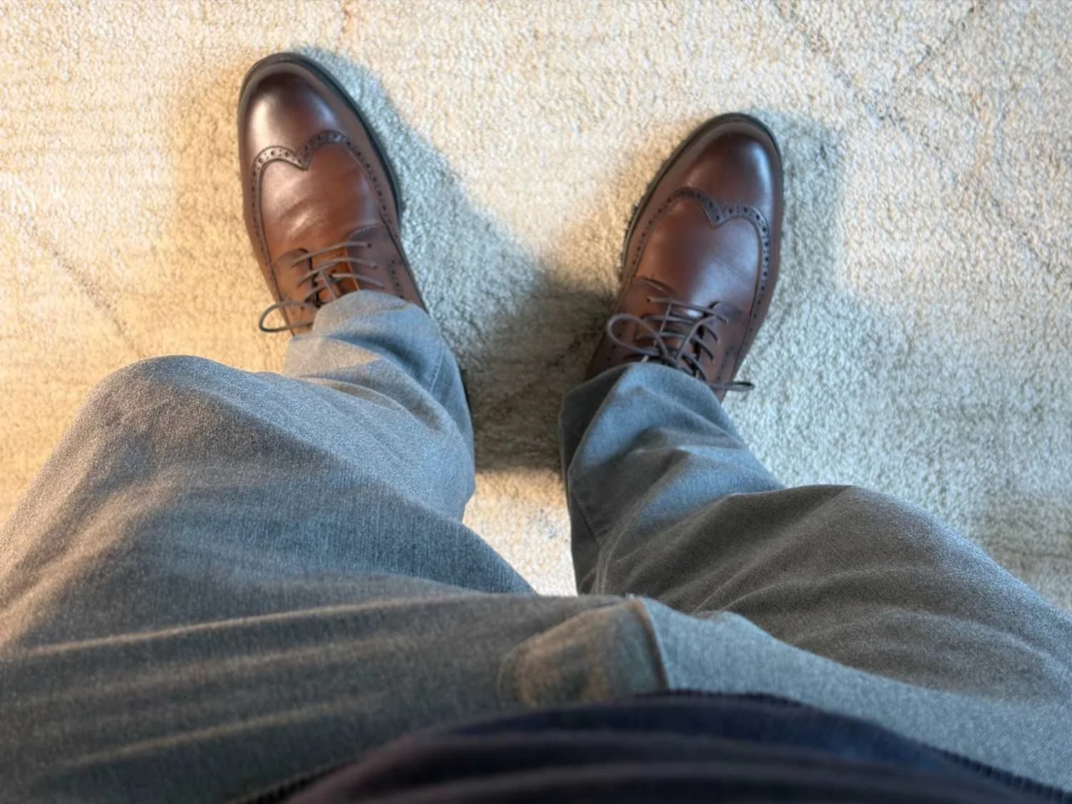 Brown Bruno Marc leather wingtip brogues worn with grey trousers, photographed from above.