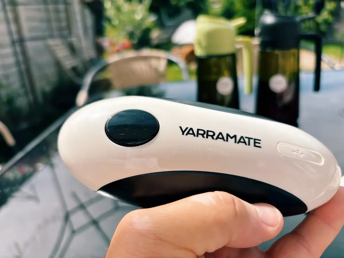 Yarramate automatic can opener shown in hand with oil and vinegar sprayer bottles in the background.