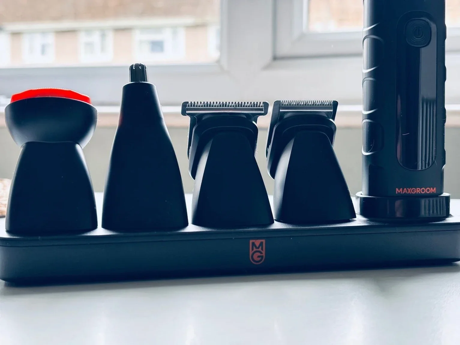 The Maxgroom body shaver docking station with various trimmer and shaver attachments on a white surface.