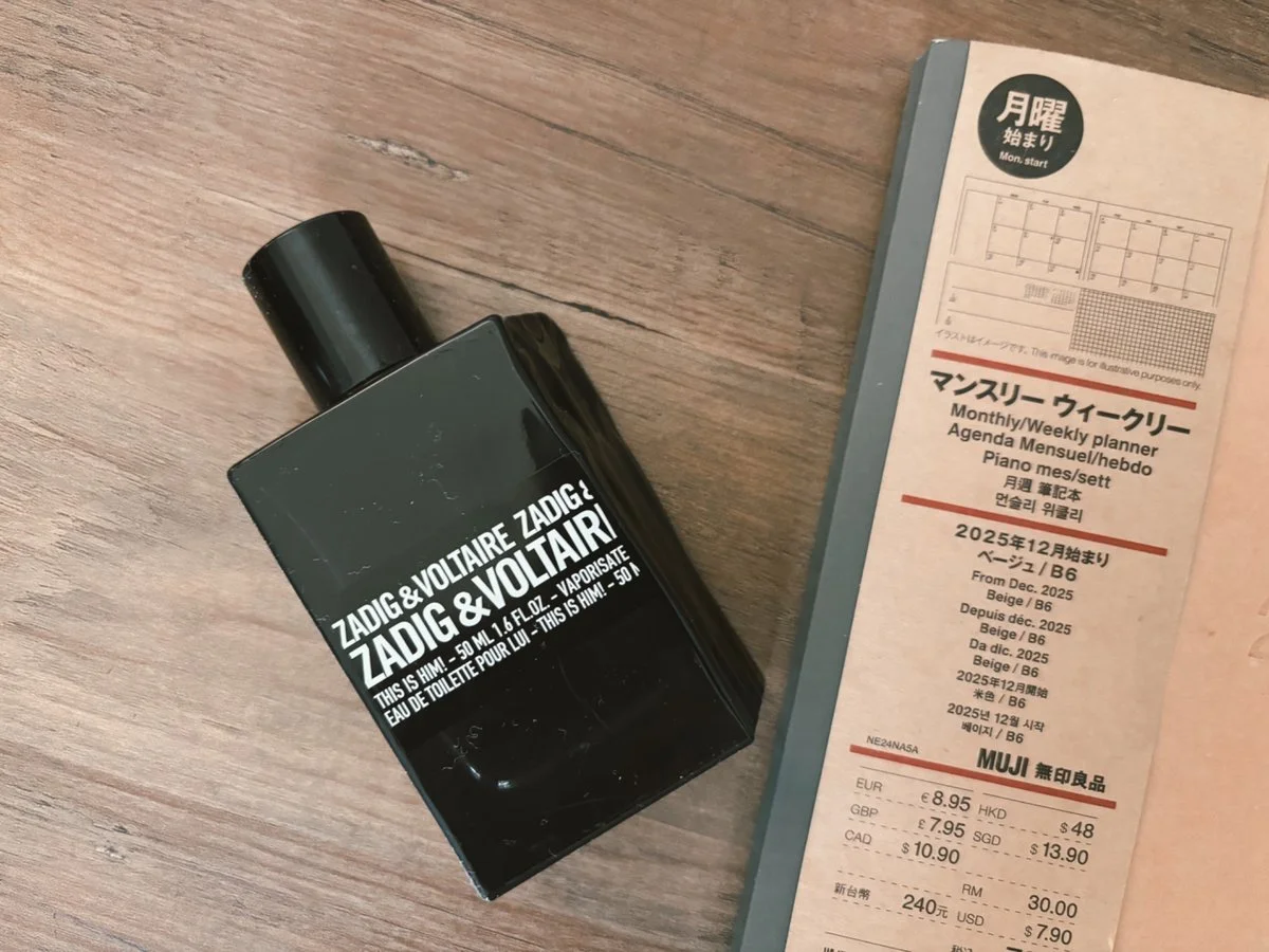 This Is Him by Zadig and Voltaire cologne bottle next to a Muji planner on wooden desk
