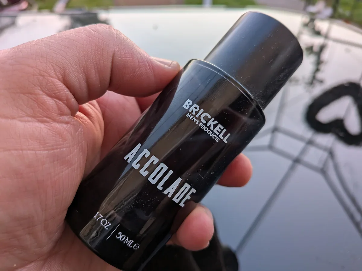 Close-up of Brickell Accolade men’s fragrance bottle held outdoors.
