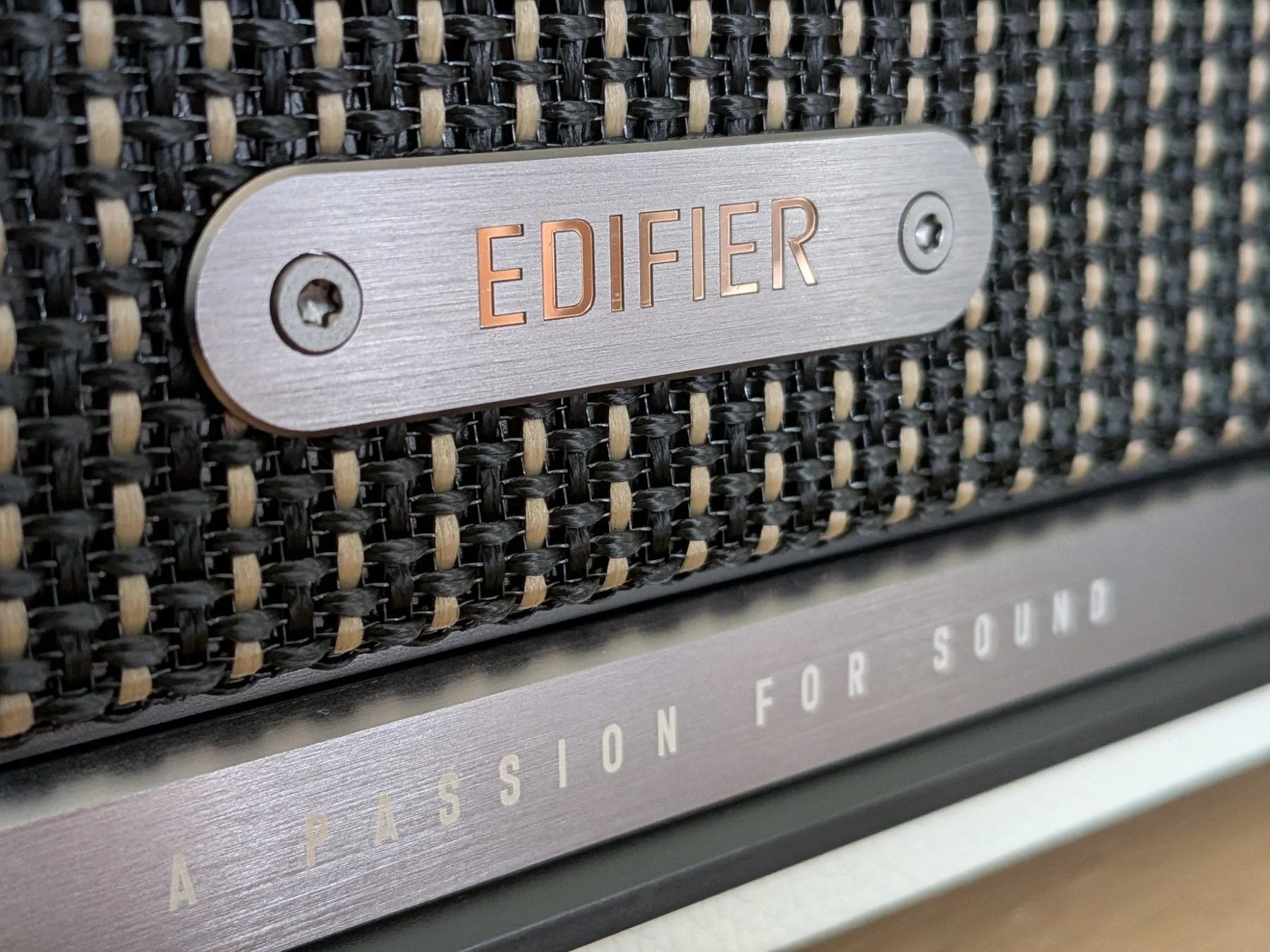Macro photo of the Edifier S300 logo badge and woven speaker grille highlighting the speaker’s premium retro design.