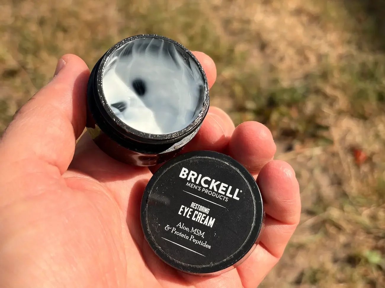 Open pot of Brickell Restoring Eye Cream held outdoors, showing the cream’s lightweight texture.