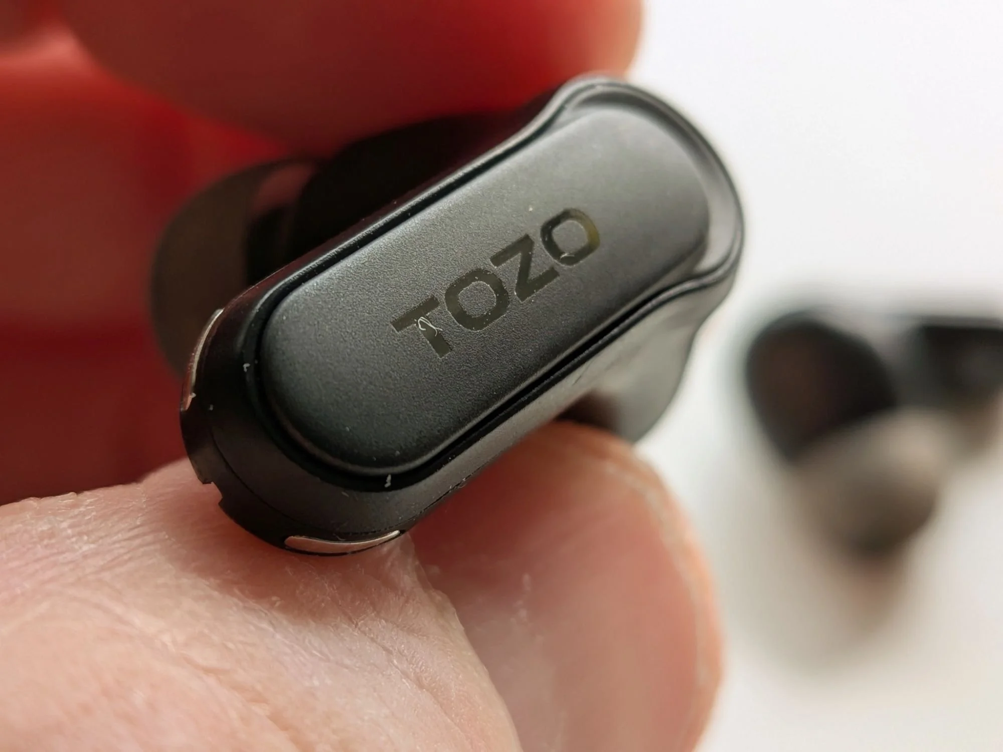 Macro detail shot of the TOZO NC20 Pro earbud, focusing on the outer shell finish and TOZO branding.