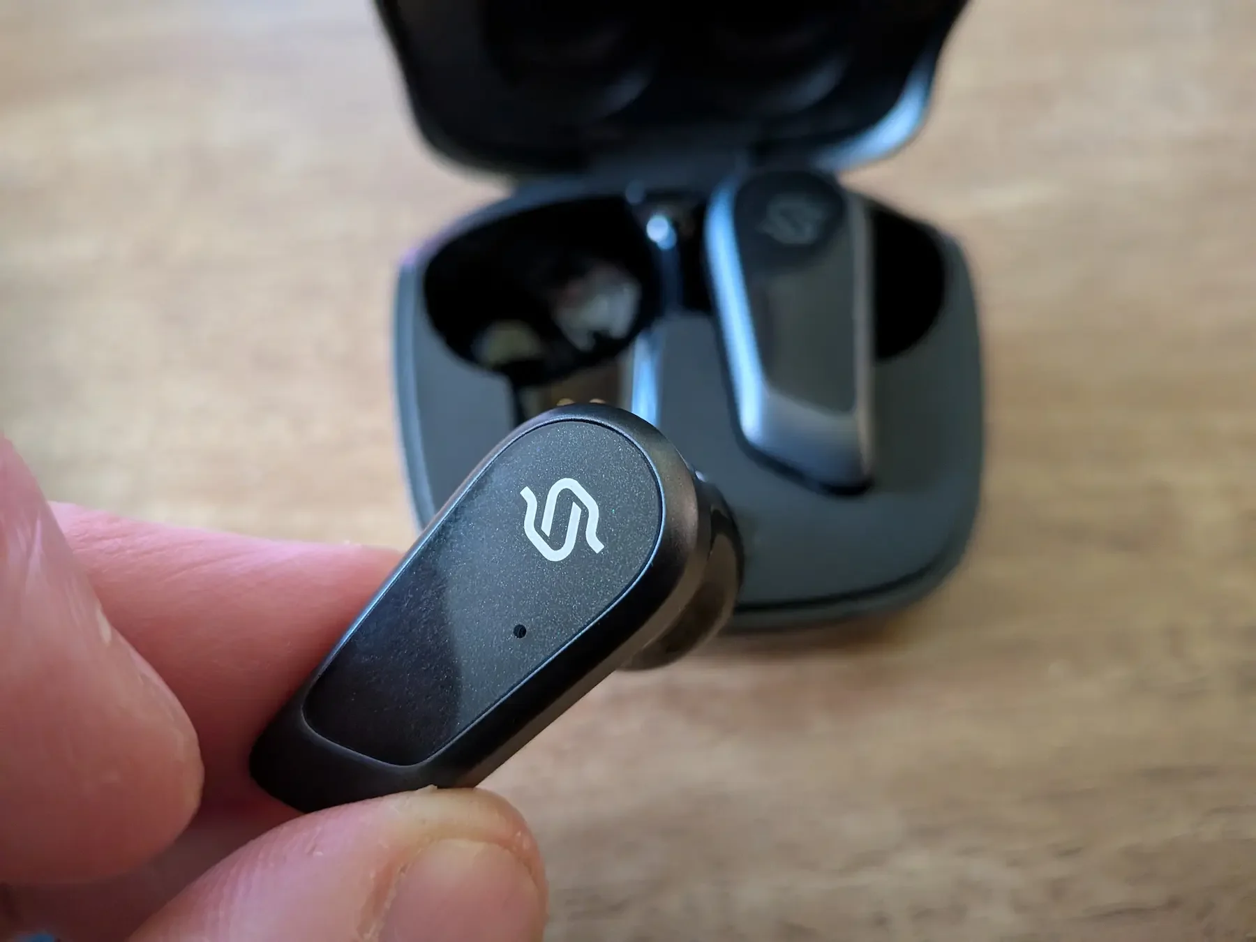 Close-up of a single Edifier STAX Spirit S10 earbud with the charging case in the background