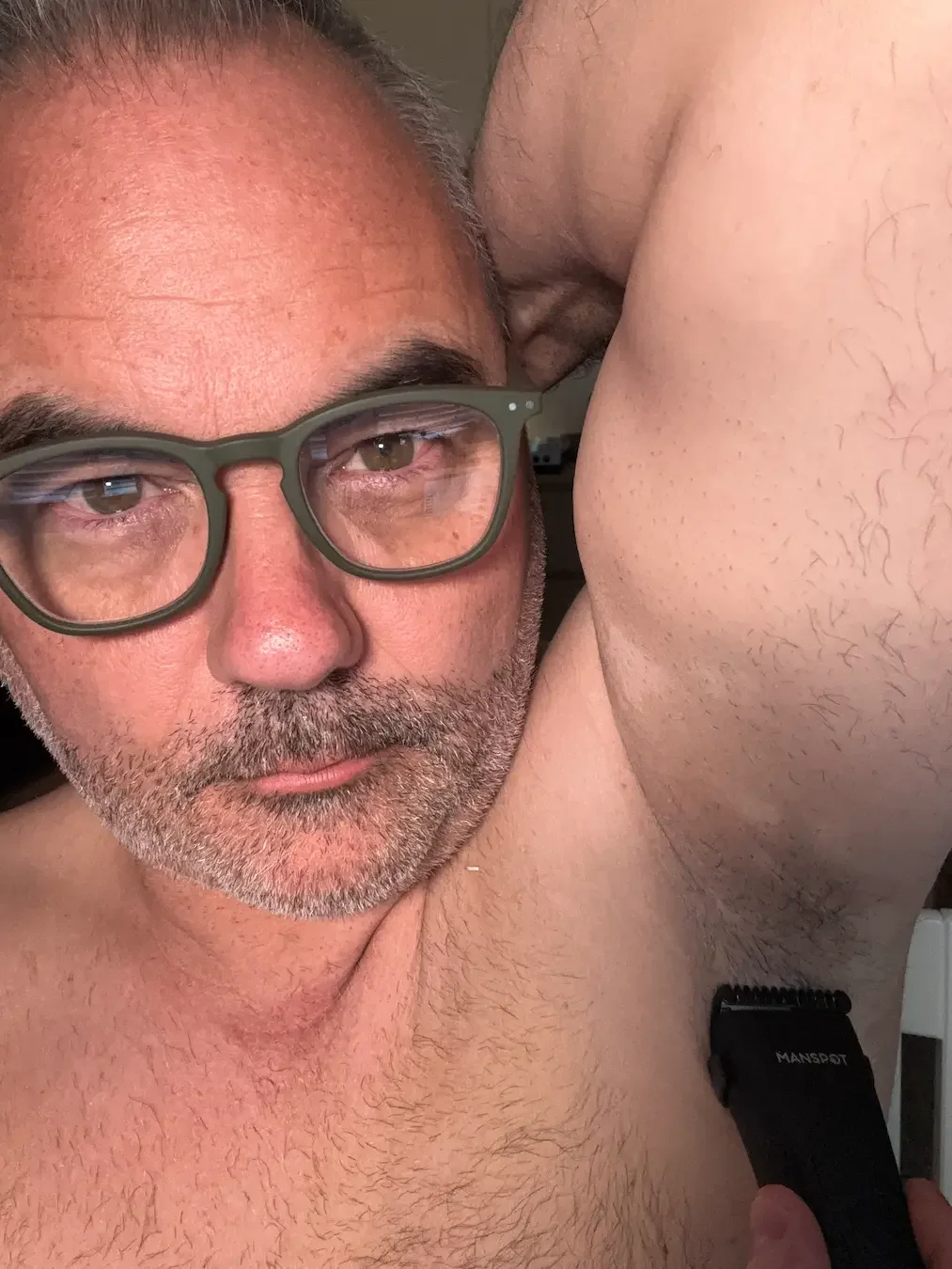 A close-up of Jerome using the Manspot trimmer to groom underarm hair, demonstrating the blade's maneuverability and skin safety.