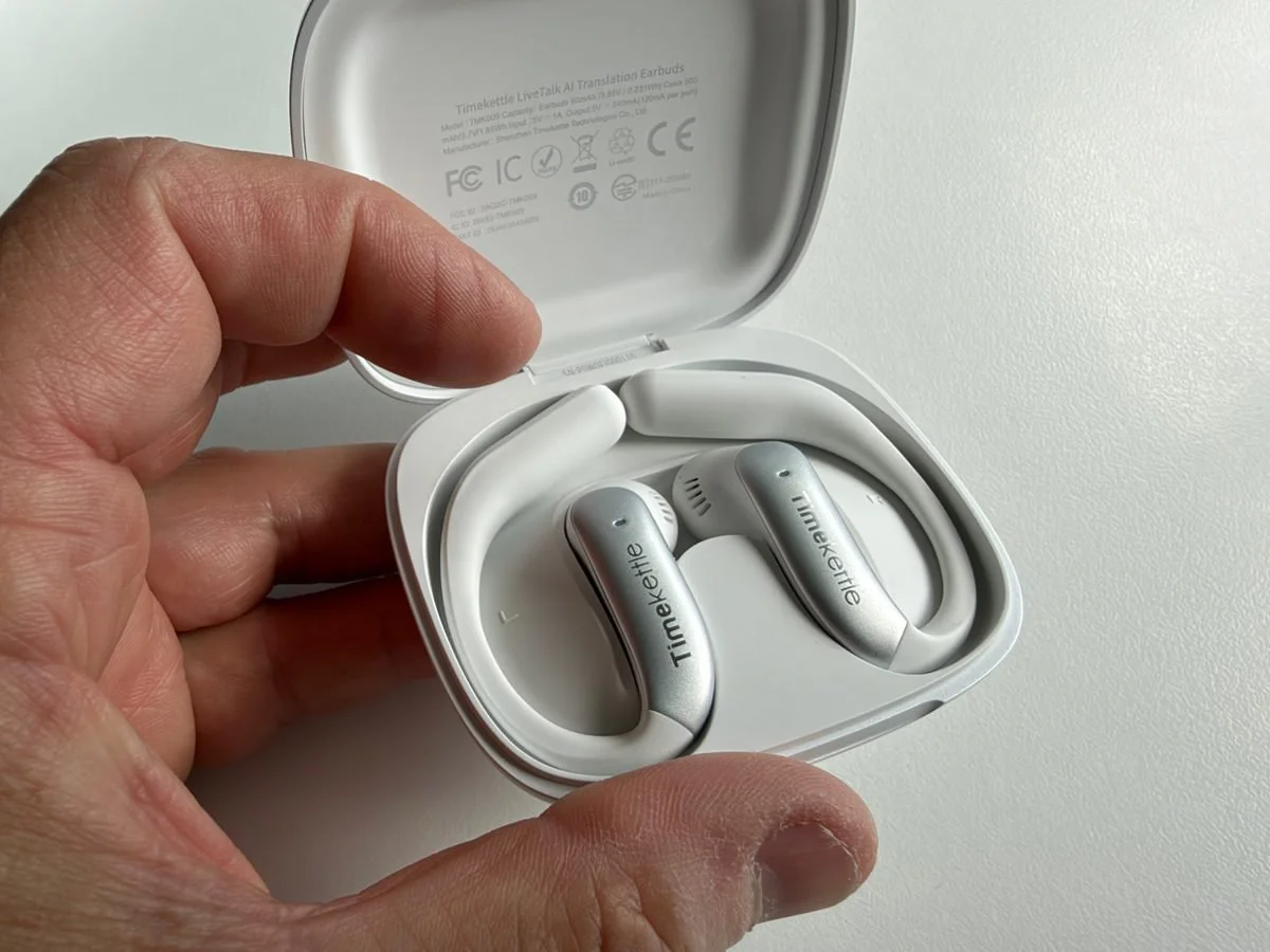 Timekettle LiveTalk AI Translation Earbuds inside their open white charging case, showing the silver finish and curved ear hooks.