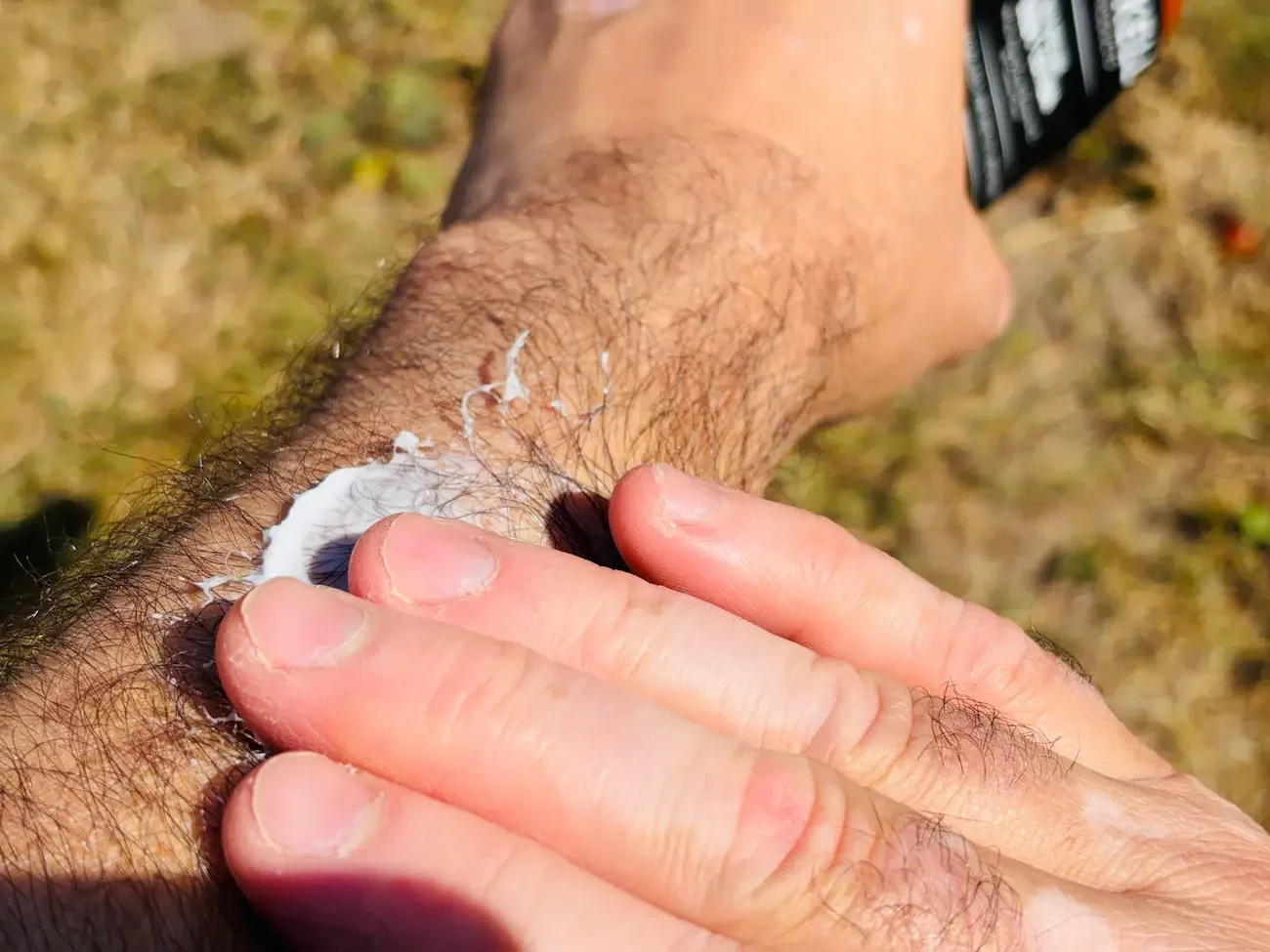 Applying Brickell Deep Moisture Body Lotion to an arm outdoors in bright summer sunshine.