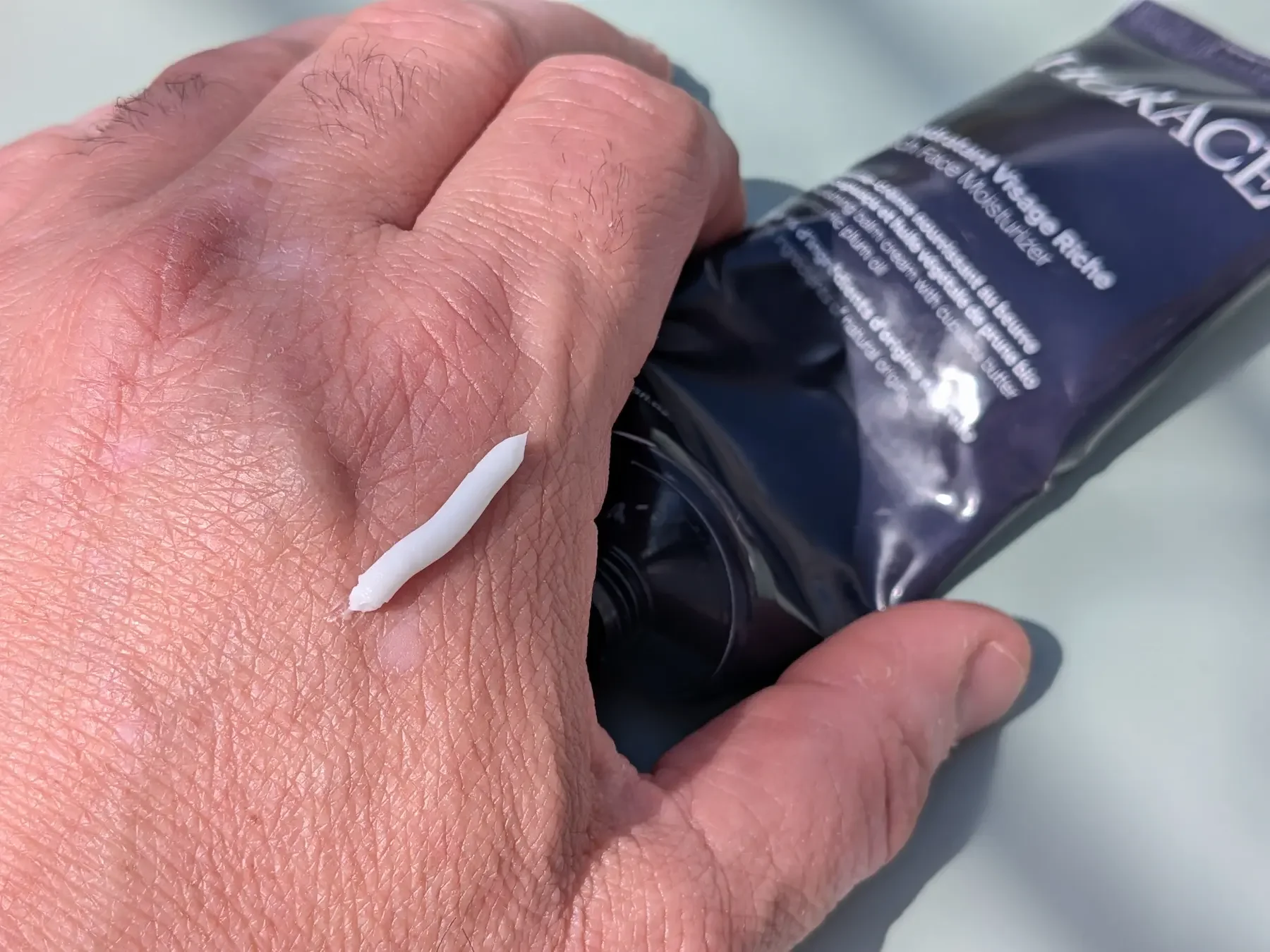 Close-up of the Horace Rich Face Moisturizer texture on the back of a hand beside the product tube.