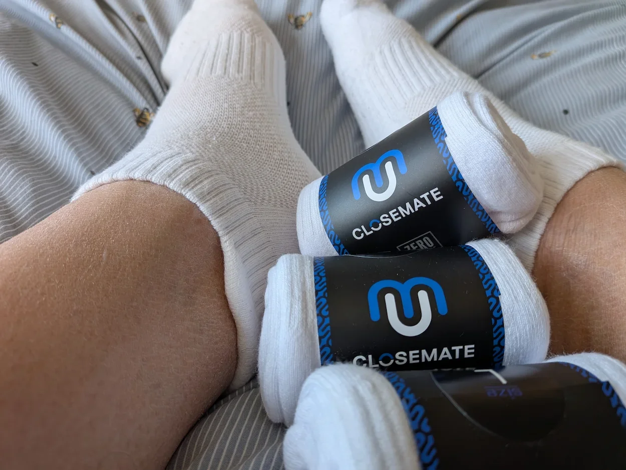 White Closemate trainer socks worn on feet showing cushioned ankle design and branded packaging.