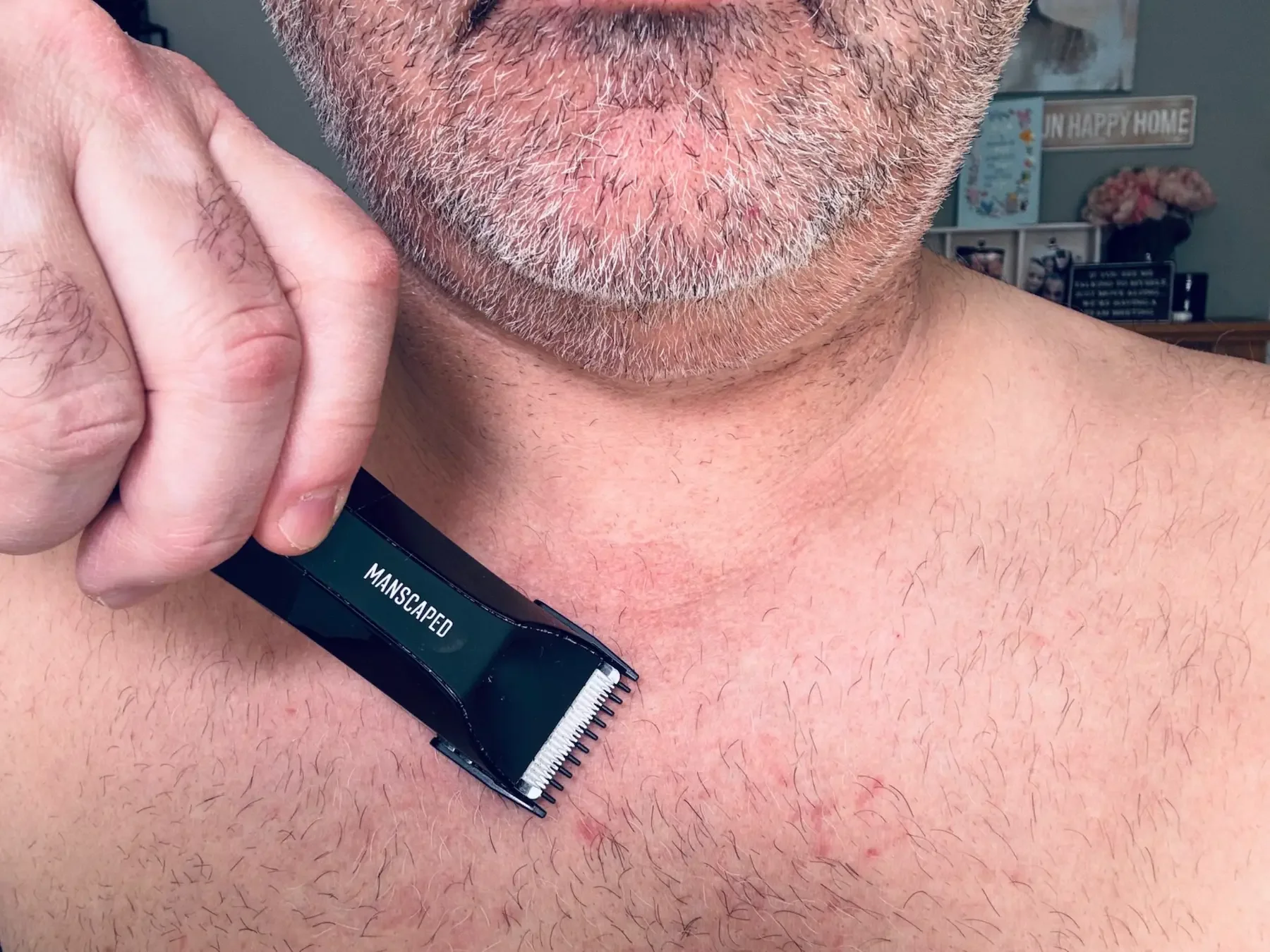 A close-up photograph of Jerome, the author of Dapper & Groomed, holding and using the Manscaped Lawn Mower 5.0 Ultra to trim hair on his chest.