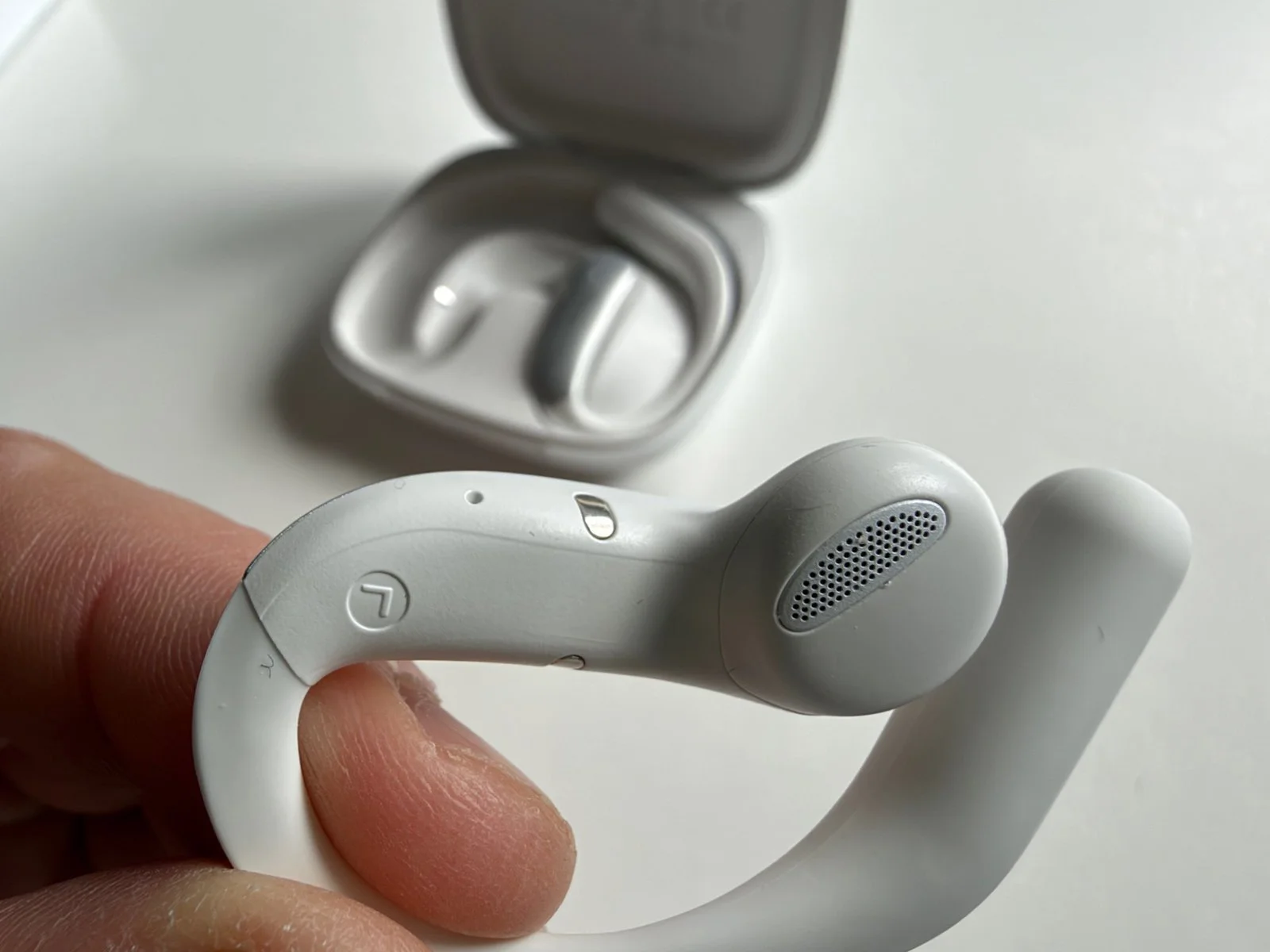 Detailed close-up of a Timekettle LiveTalk translation earbud showing the speaker grille, charging contact and curved open-ear hook