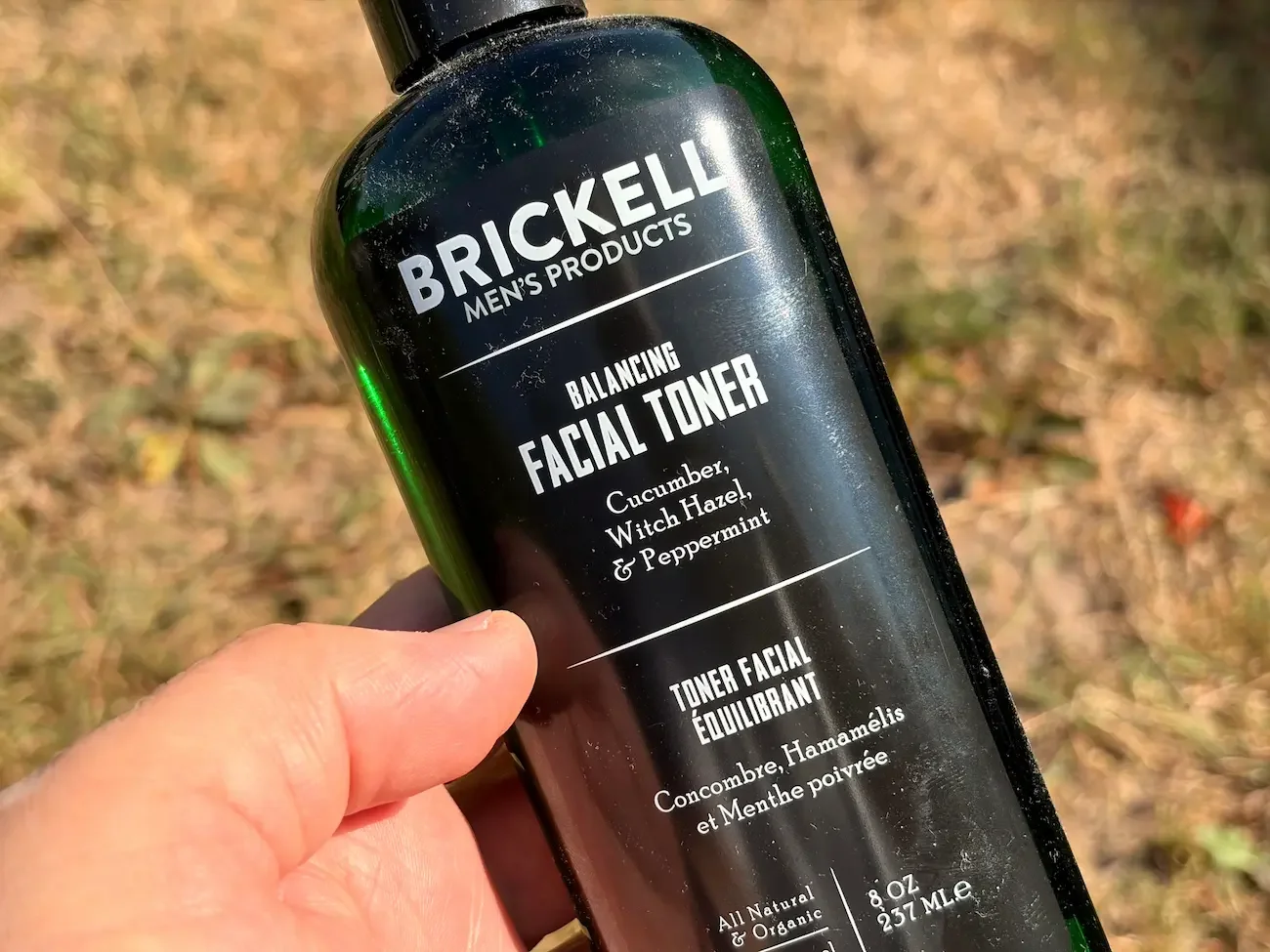 Close-up of Brickell Balancing Facial Toner held outdoors in bright summer sunshine.