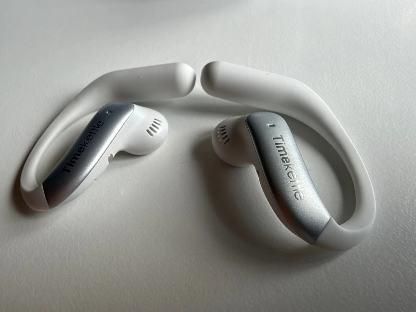 Pair of white and silver Timekettle LiveTalk AI Translation Earbuds resting on a white surface, showing their open-ear design.