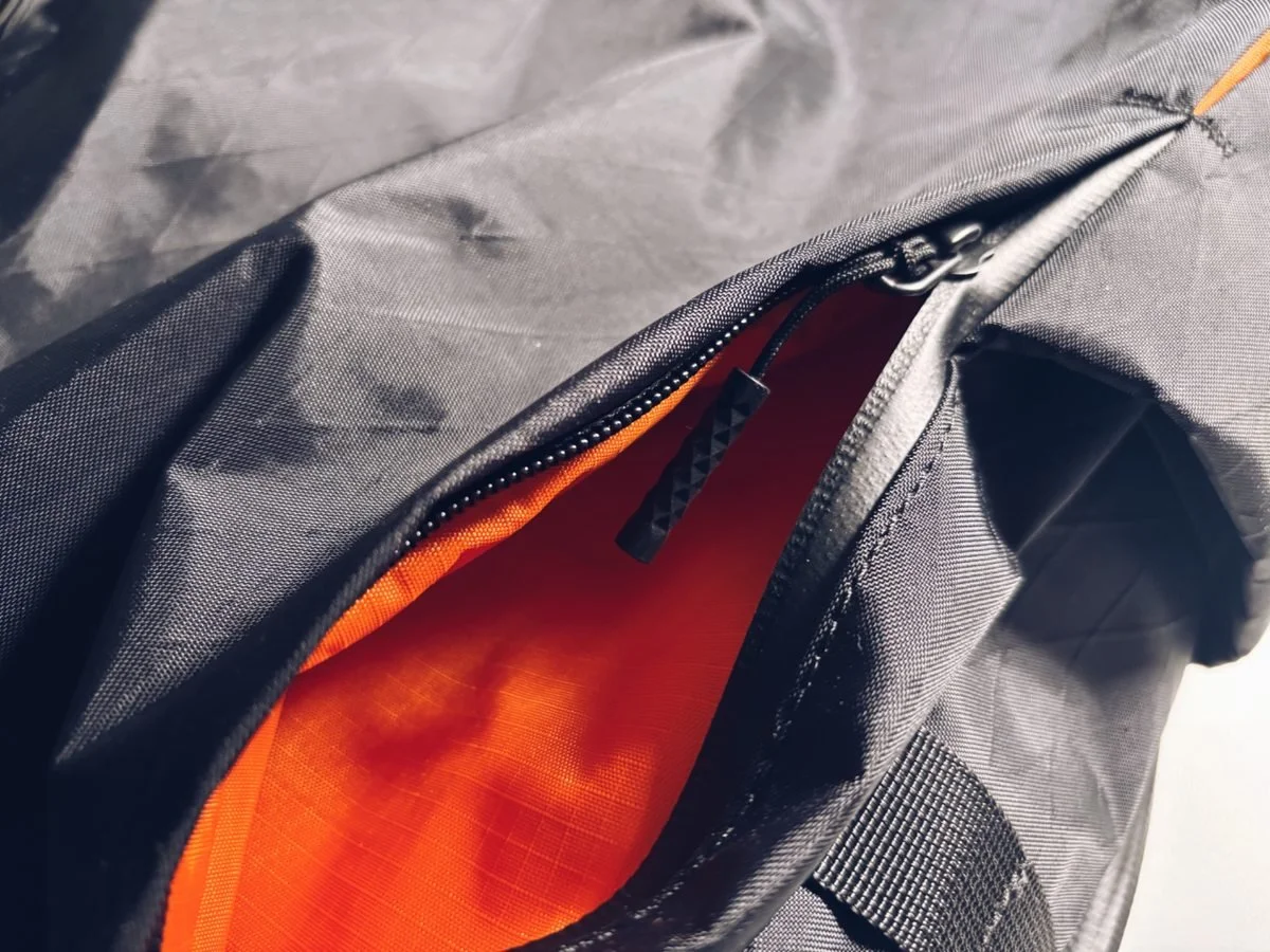 Close-up of the ADD1D D2D Essential Backpack front pocket with high-visibility orange lining and zip detail for quick-access storage.