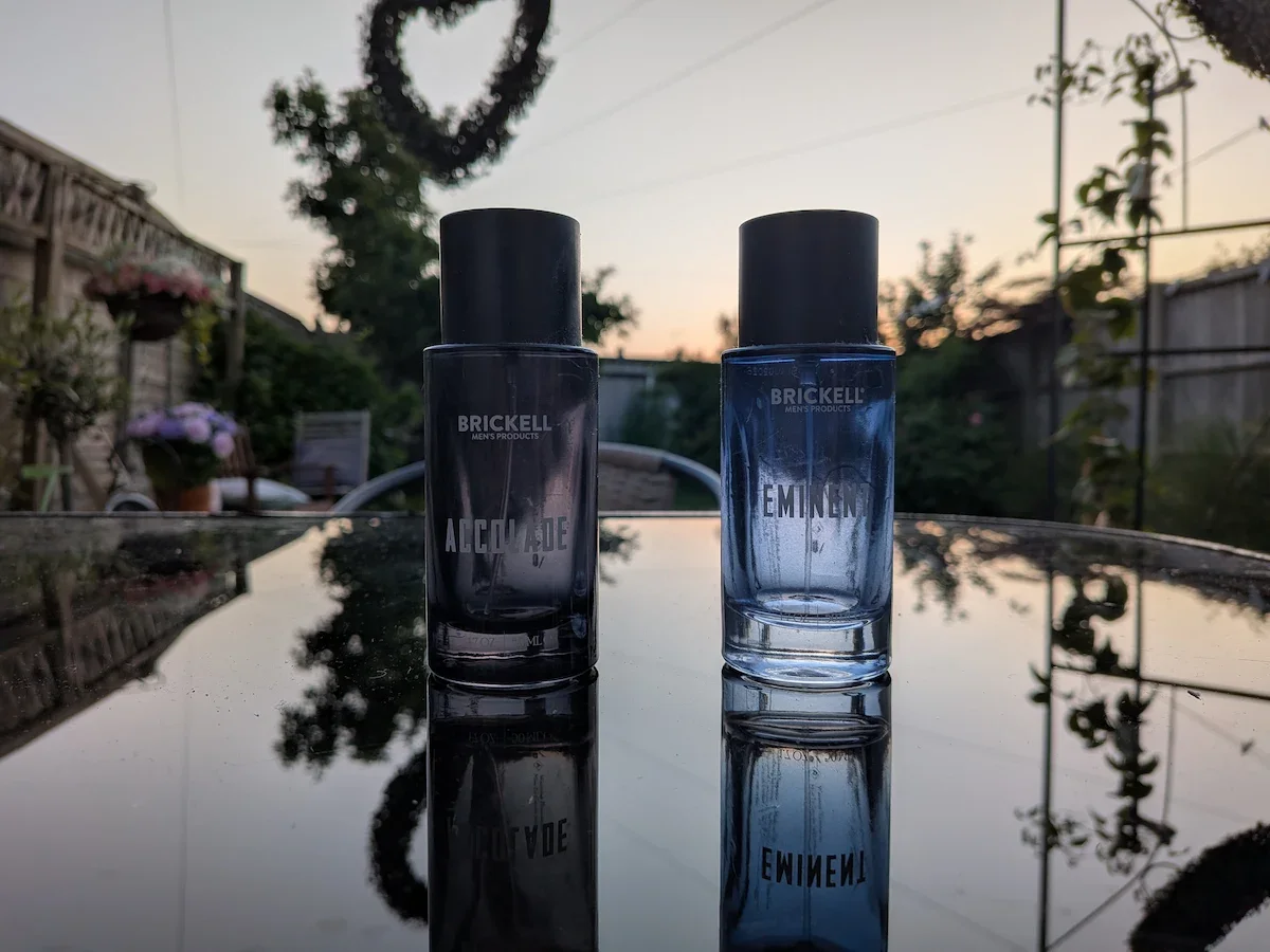 Brickell Accolade and Eminent men’s fragrances on a glass garden table at sunset.
