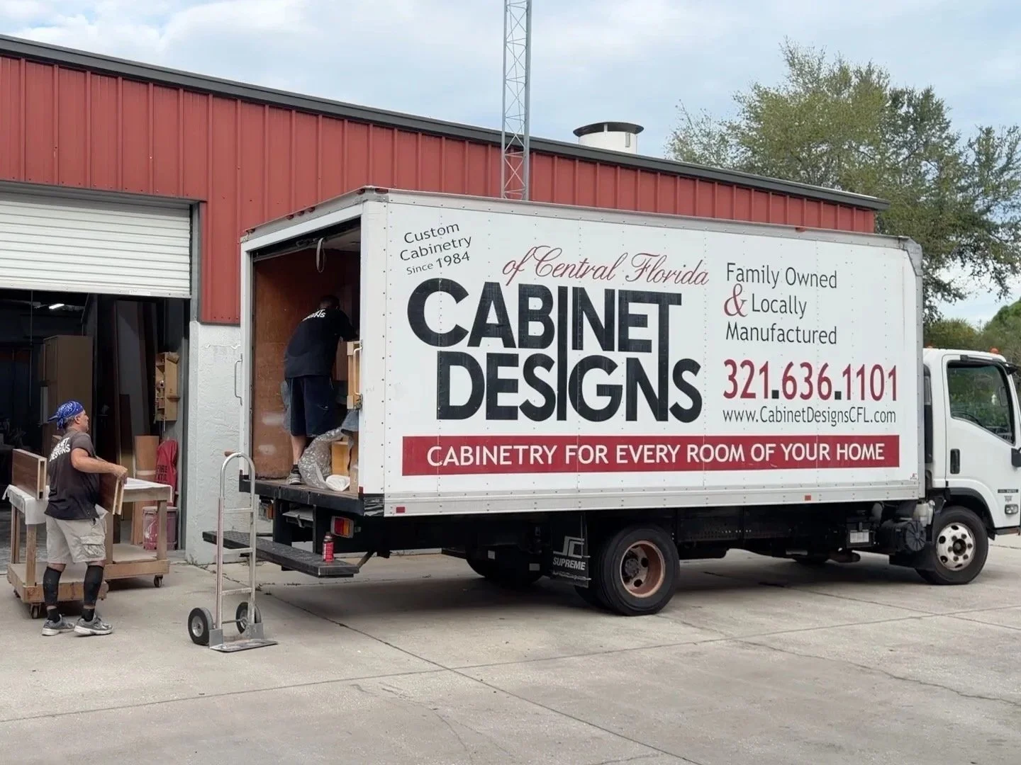 A moving truck with advertisement for Central Florida Cabinet Designs being unloaded outside a building, with two workers carrying cabinets.