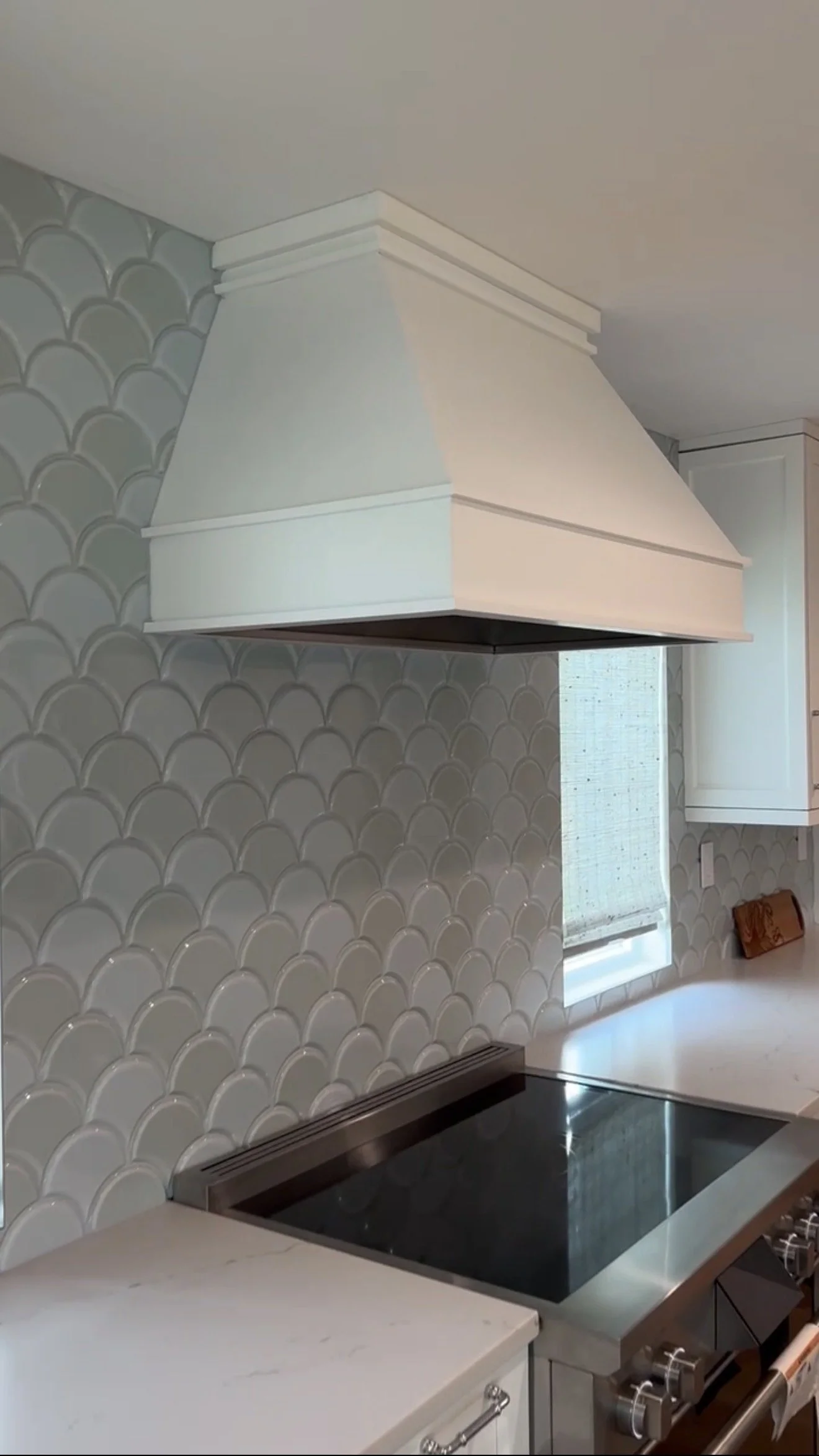 Kitchen with white range hood, grey scallop tile backsplash, white cabinets, and a black stove.