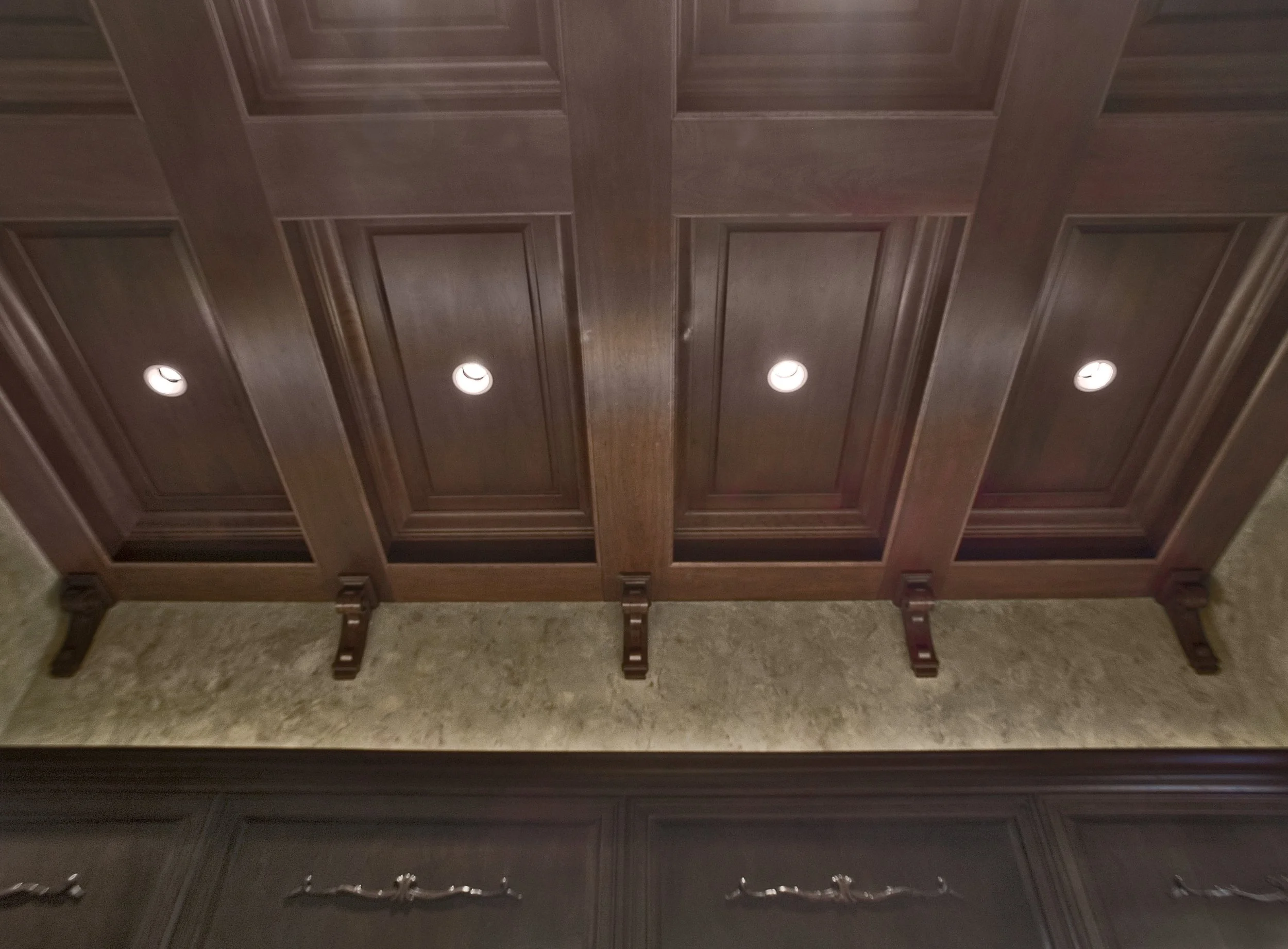 A wooden ceiling with recessed lighting and a wooden cabinet or panel below.