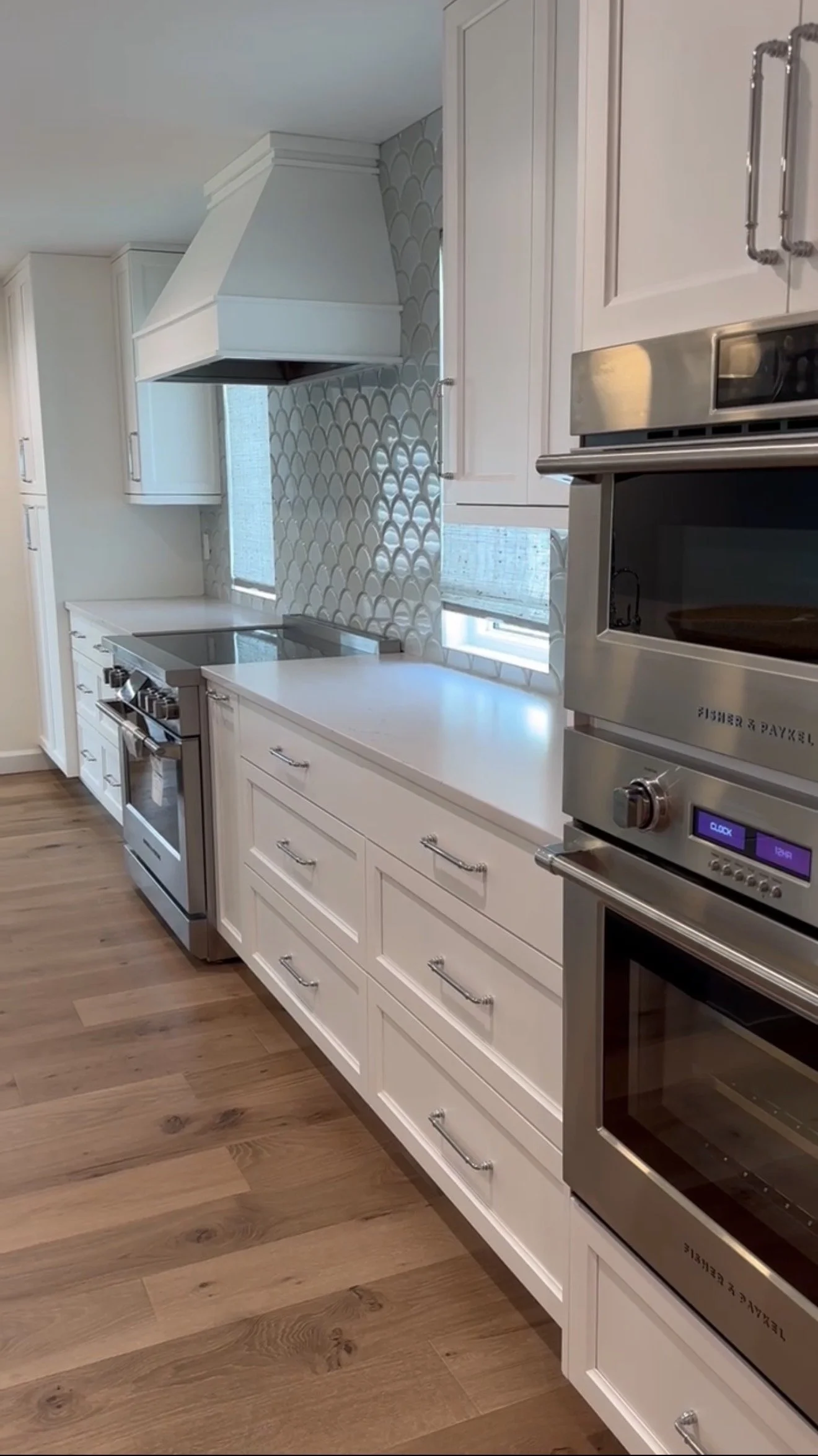 Modern kitchen with white cabinets, stainless steel appliances, wooden floor, and a decorative backsplash.