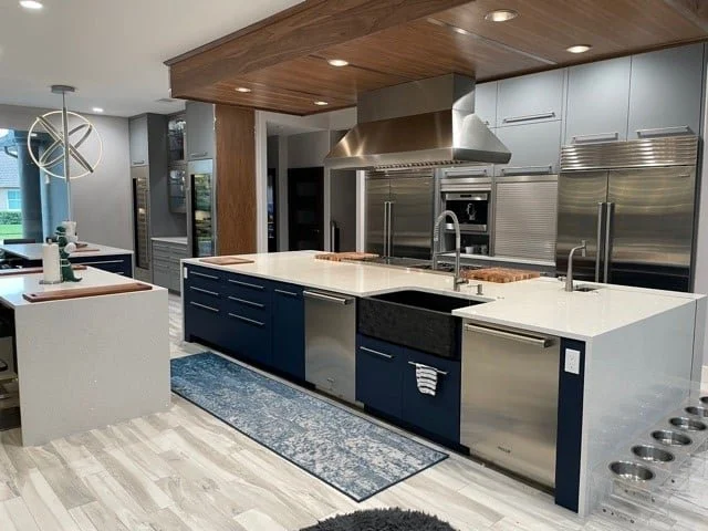 Modern kitchen with blue cabinetry, white countertops, stainless steel appliances, wooden ceiling, and a patterned rug.