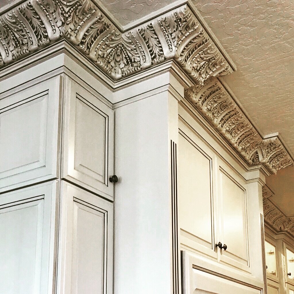 Close-up of ornate crown molding and cabinet in a kitchen, painted in a light color.