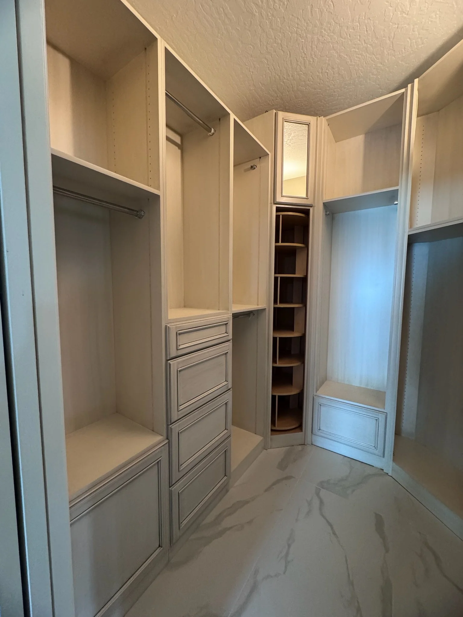 Empty walk-in closet with built-in shelves, drawers, and hanging rods, illuminated by natural light from an unseen window.