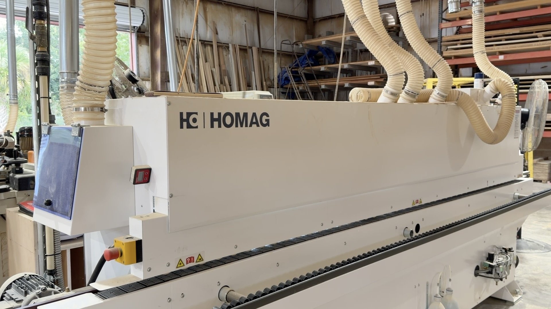 Woodworking CNC machine in a woodshop with shelves of wood planks in the background.