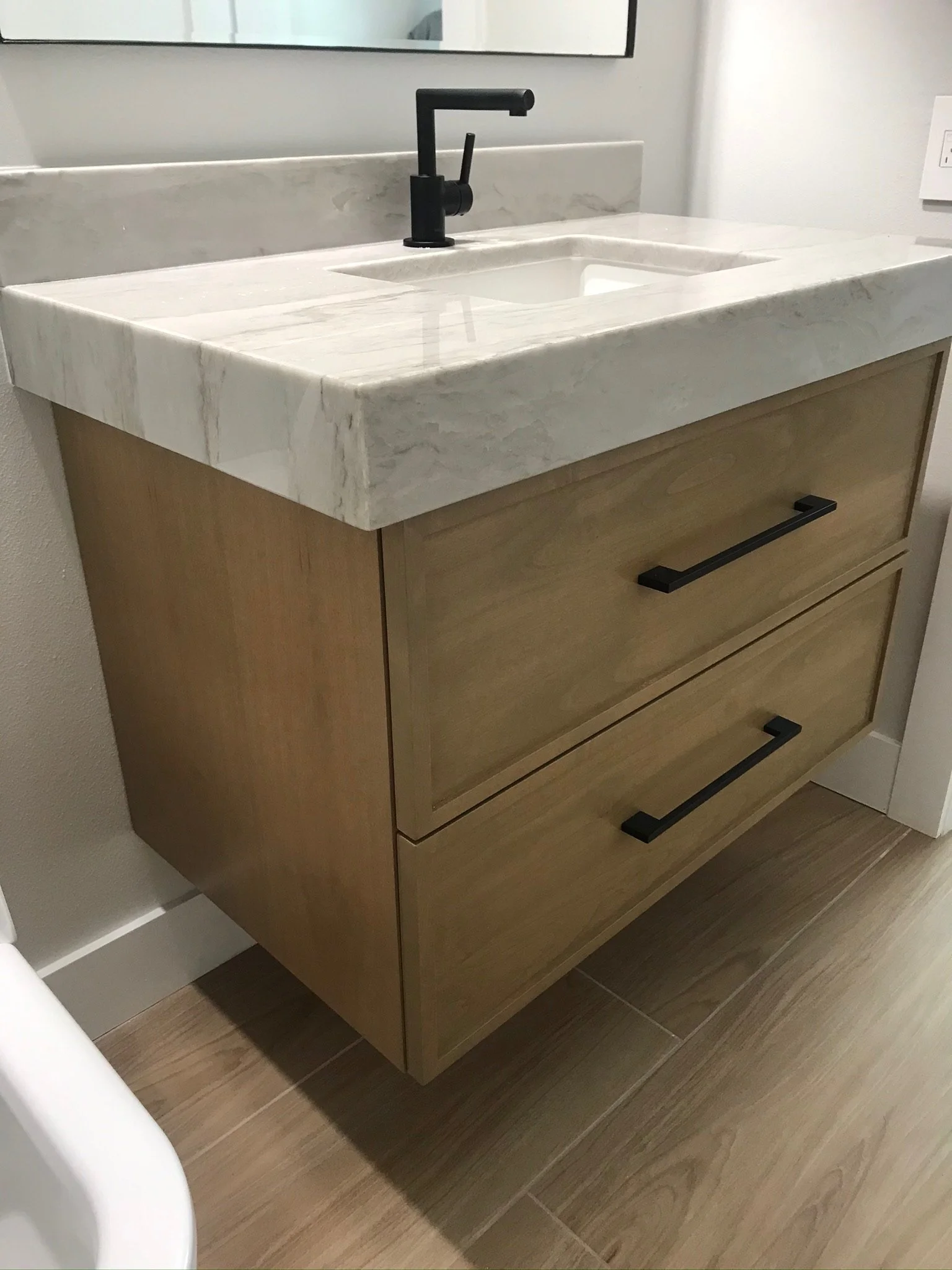 Modern bathroom vanity with a white marble countertop, black faucet, and wooden cabinet drawers with black handles.