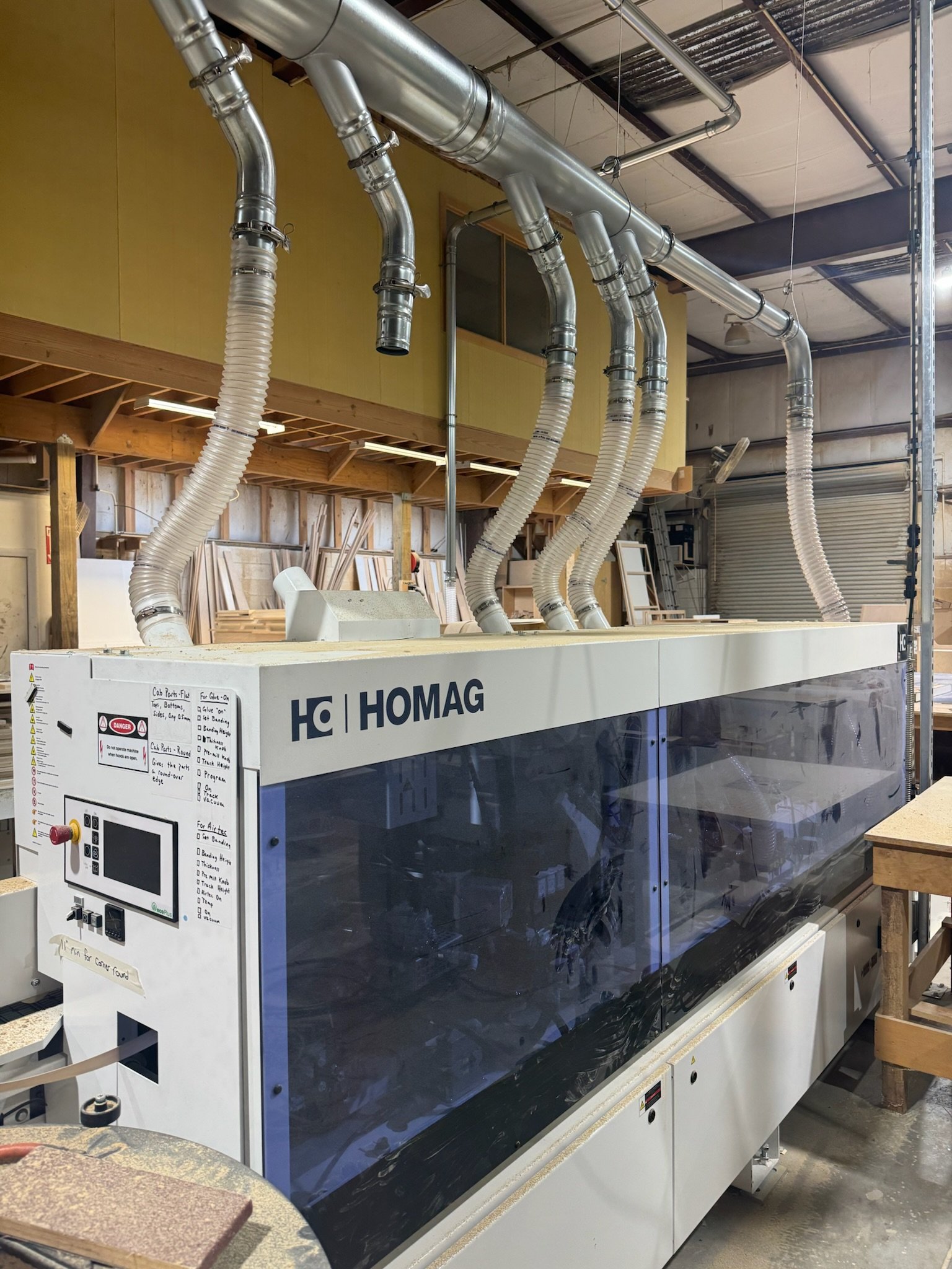 Industrial dust collection system with silver pipes and flexible hoses in a workshop or manufacturing space.