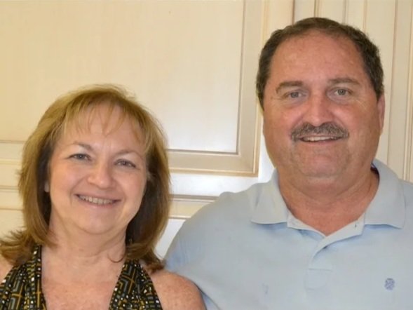 A smiling middle-aged woman with shoulder-length blonde hair and a man with short dark hair and facial hair, both posing indoors.