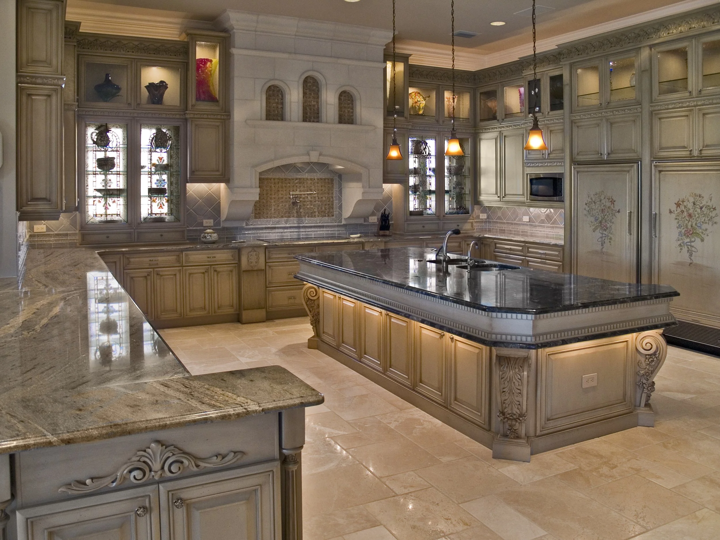 A luxurious kitchen with cream-colored cabinets, a dark granite island, and ornate architectural details. The kitchen features stained glass windows, decorative vases, and pendant lights hanging from the ceiling.