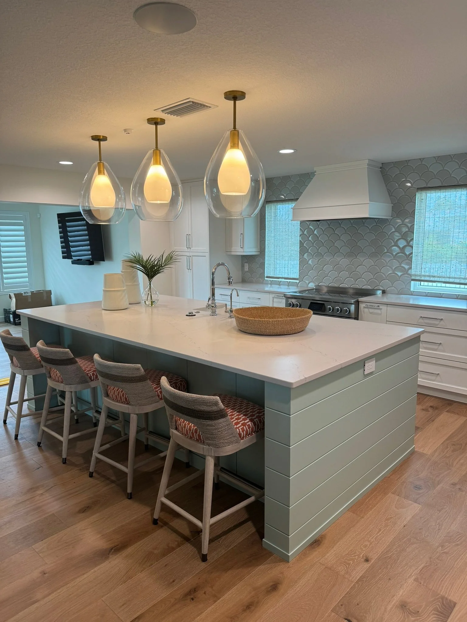 Modern kitchen with a large island, pendant lights, white cabinetry, a stove, a mosaic tile backsplash, and wooden flooring.