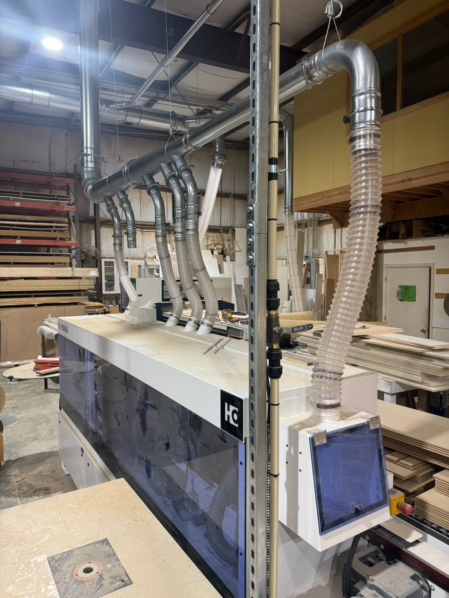 Industrial workshop with piping, a machine with a glass shield, and various construction materials.