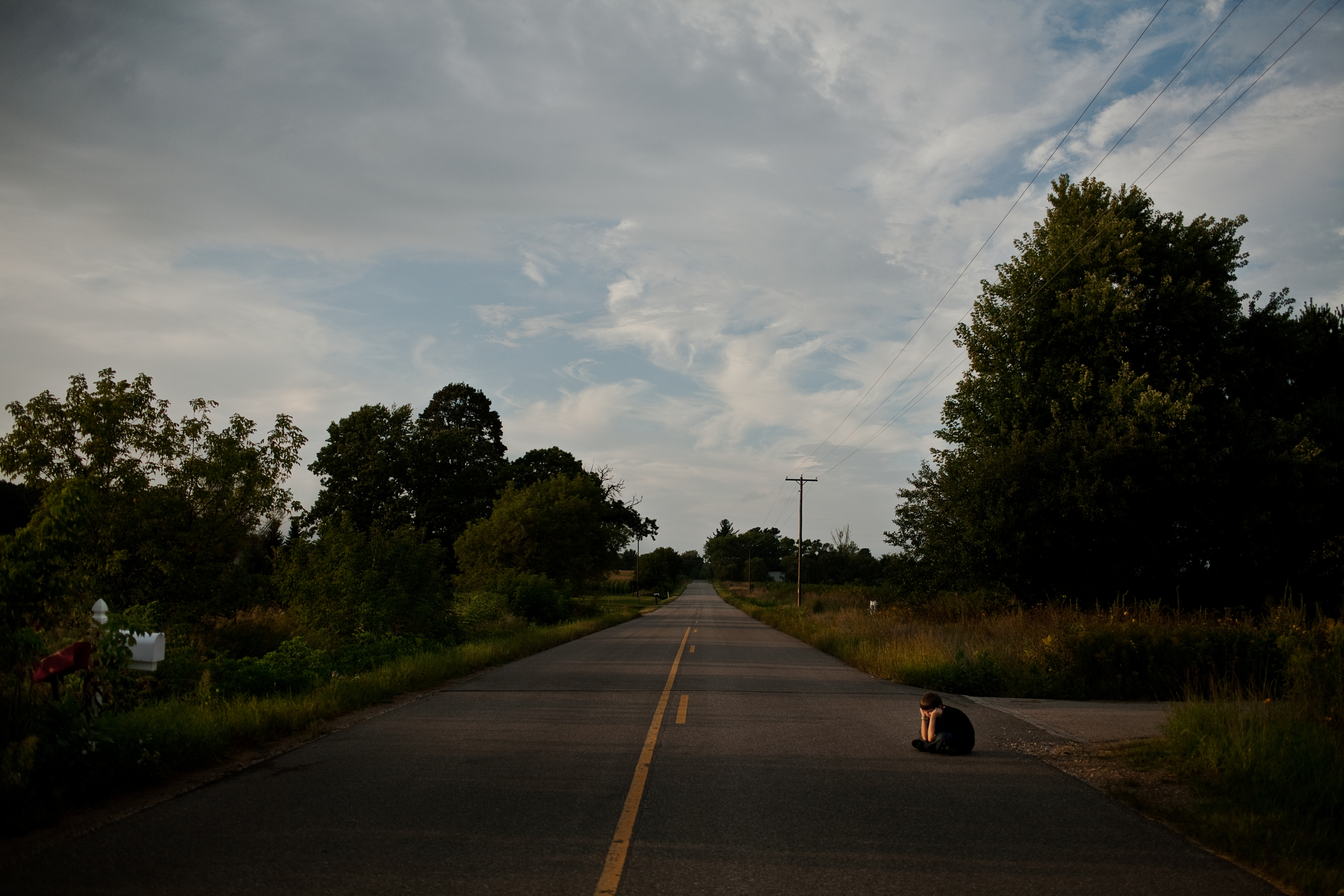  Isaac sits alone, outside his uncle's house as the sun sets over the wide open road. 