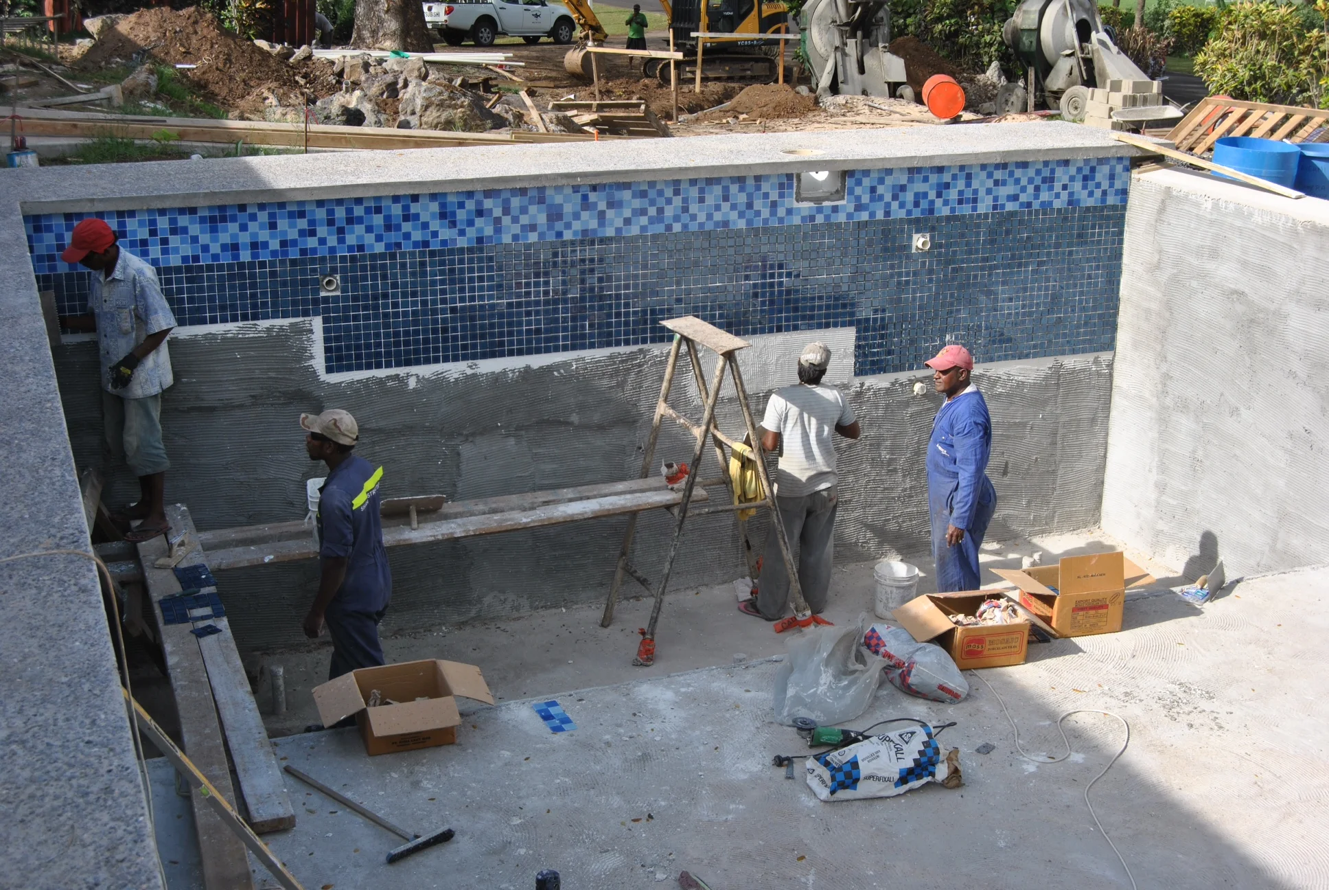 Craftsmen are working on the tiling the pool. Man, is that a lot of tiles. You can also see the infinity edge to the right of the frame, and the polished concrete edge around the lip of the pool.