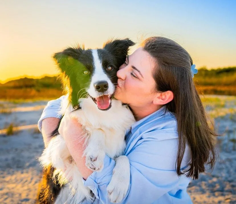 Woman hugging a black and white dog on the beach at sunset