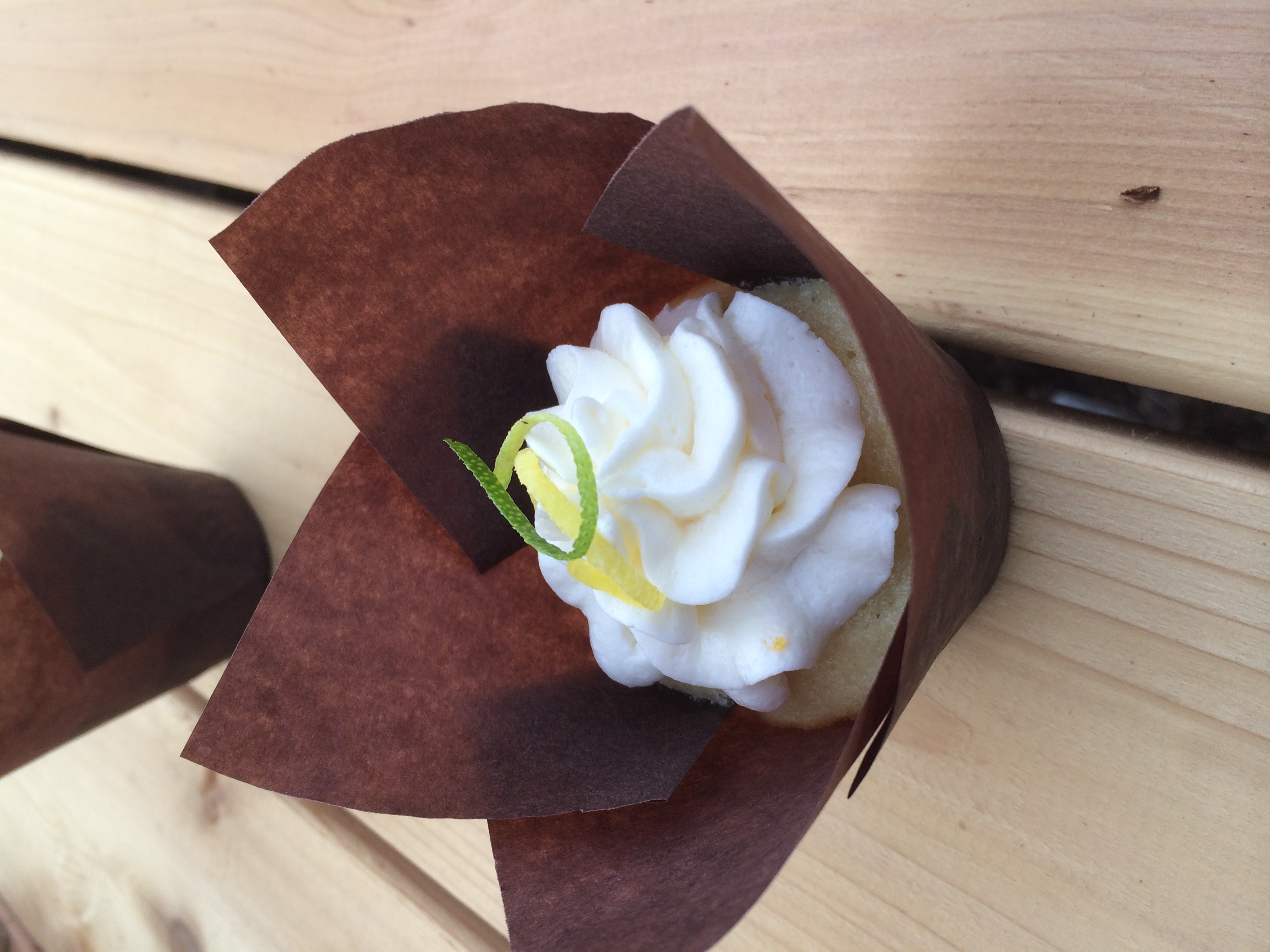 Fresh lemon cupcake filled with homemade lime curd and topped with lemon juice and zest buttercream. Garnished with a lime and lemon zest curl.
