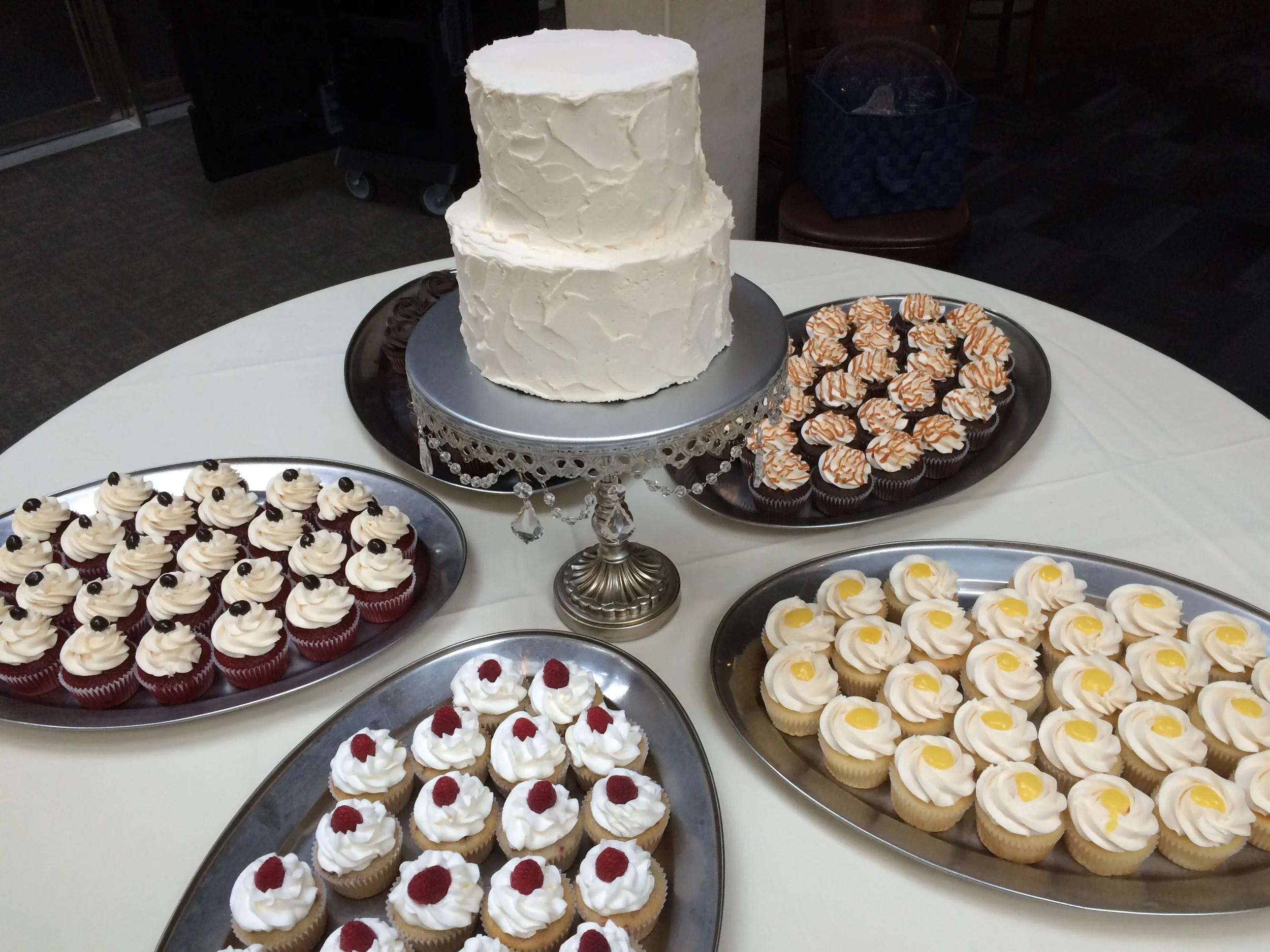 Wedding cakes, top tier is lemon and bottom tier is salted caramel, surrounded by various cupcake flavors