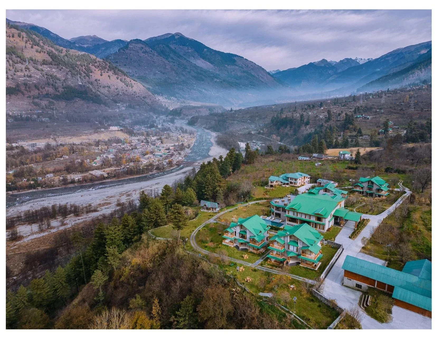 Its an aerial shot of Baragarh Resort, Manali by IHCL Seleqtions. Shot in the morning with view ofvyas river which flows through Manali. This is the hero image of the property which shows the resort location & expansive mesmerising views.