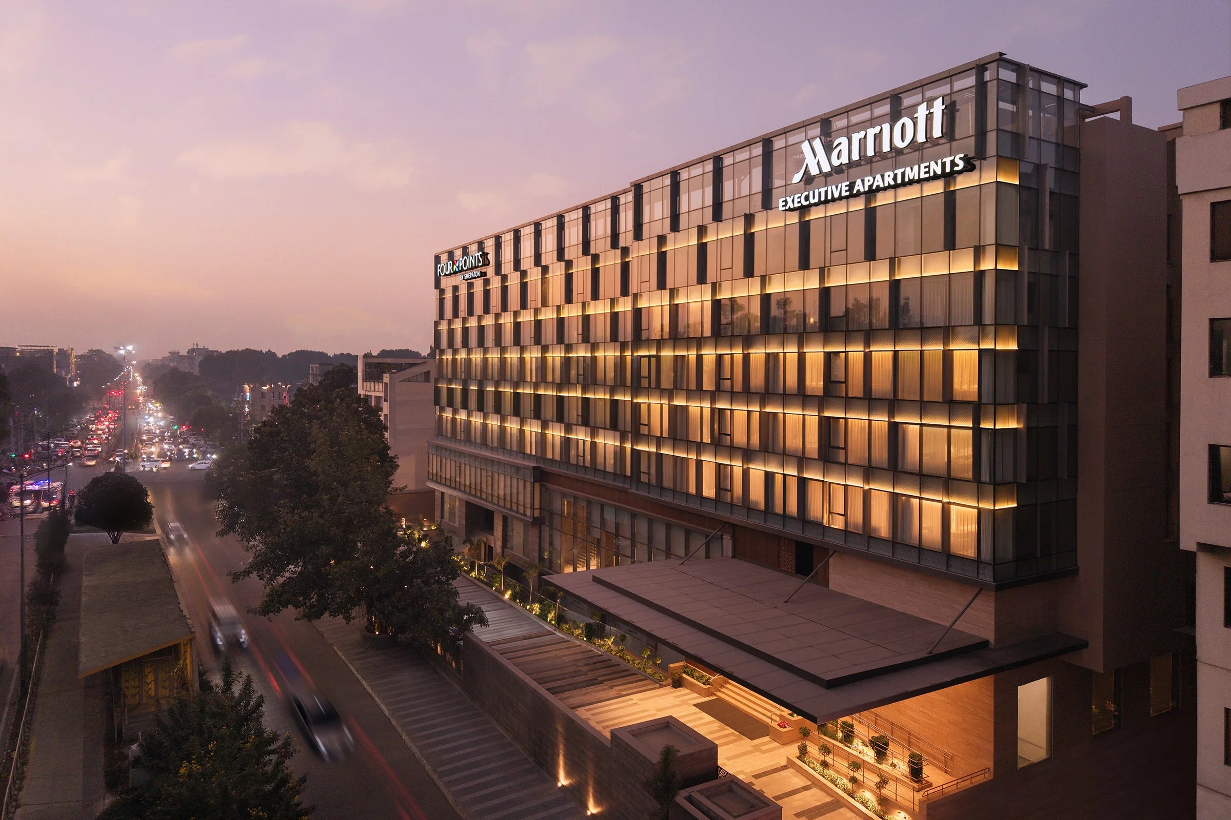 Twilight exterior of the dual-branded Four Points by Sheraton and Marriott Executive Apartments building in Amritsar, glass façade glowing warm against a dusk sky.