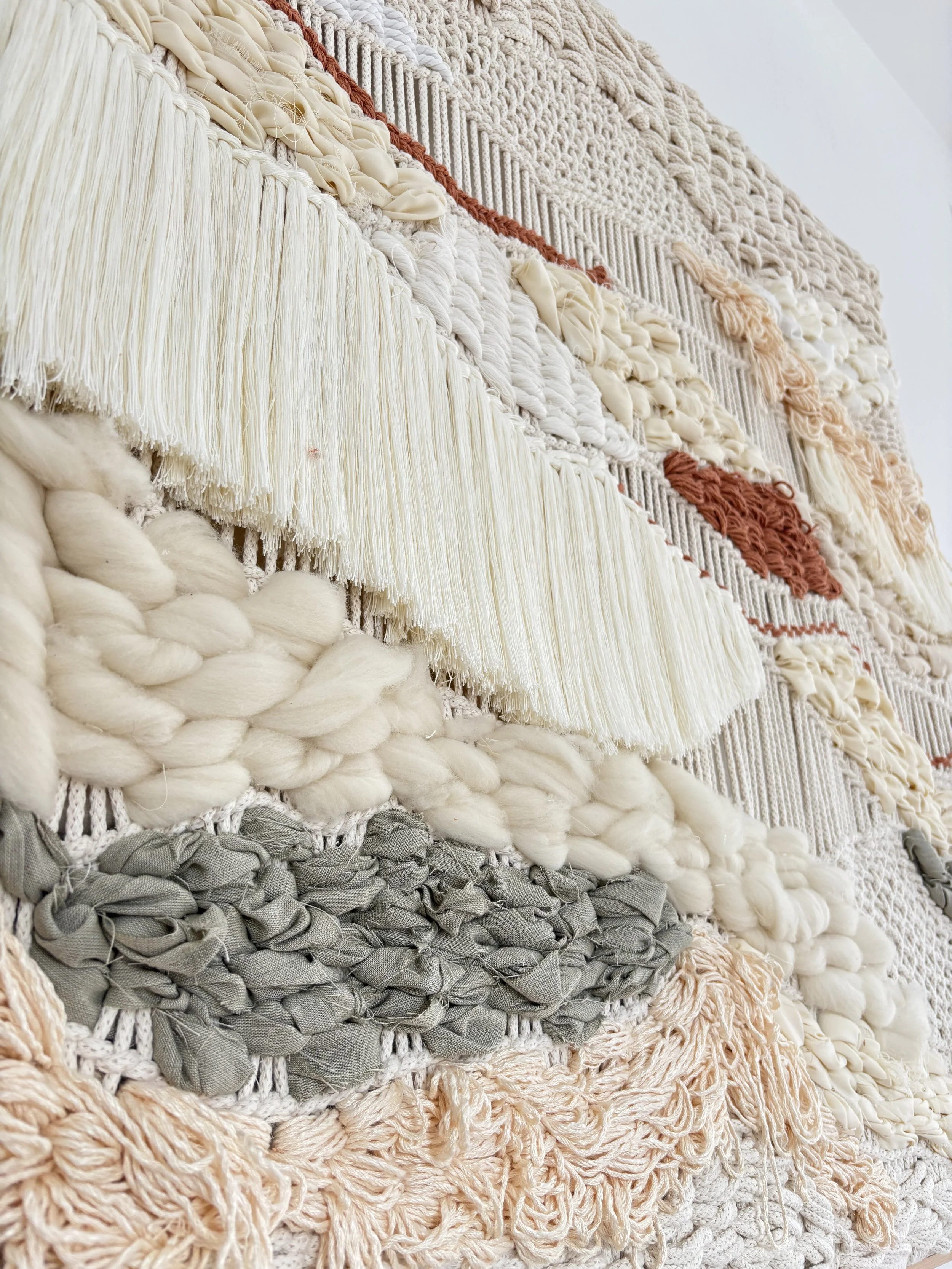 Framed textile wall art with layered natural fiber in earth tones, handwoven with dimensional texture, displayed on white wall