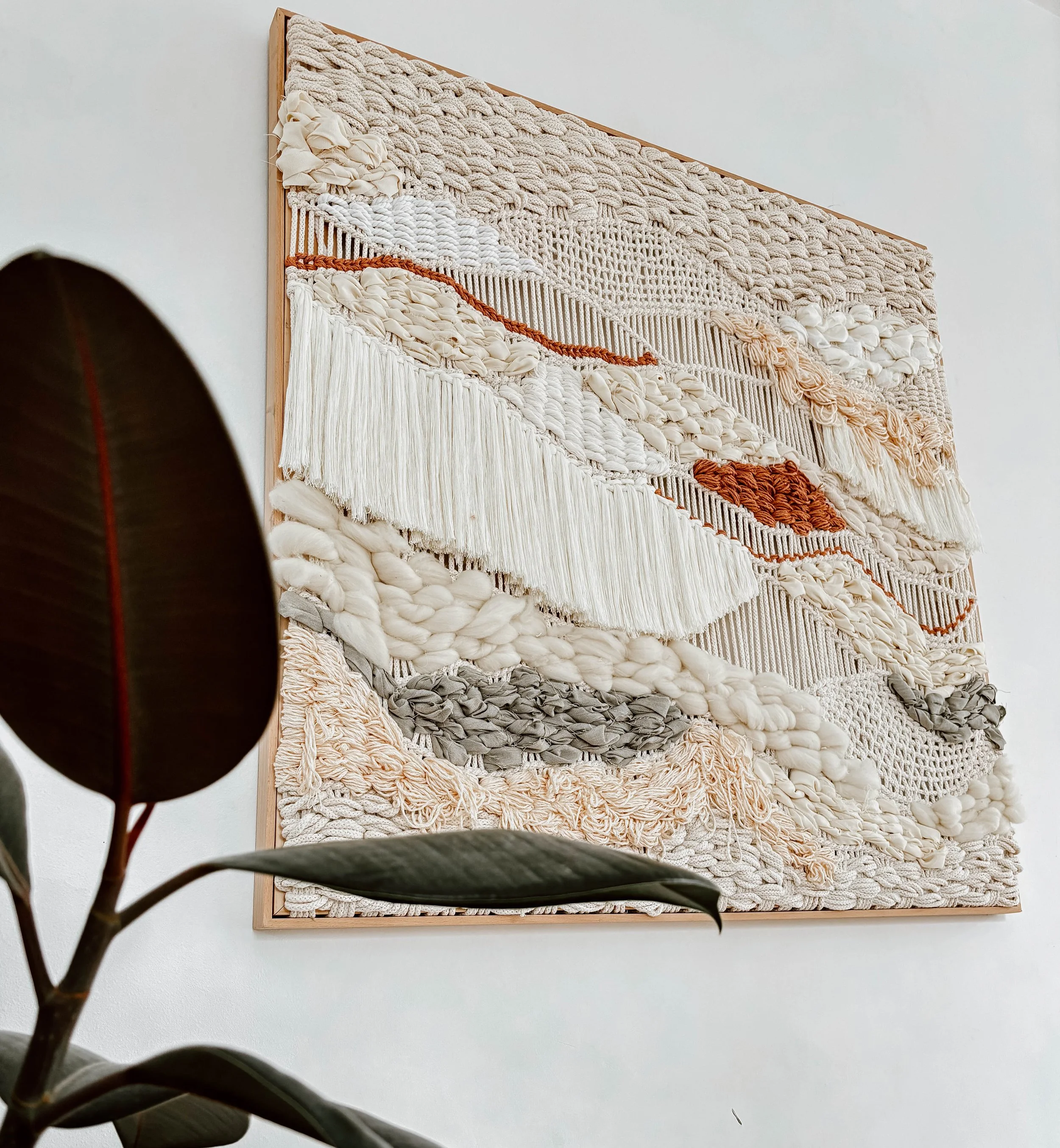 Framed textile wall art with layered natural fiber in earth tones, handwoven with dimensional texture, displayed on white wall