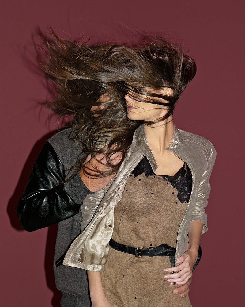 Fashion photoshoot with models posing against a red background, hair blown across their faces.