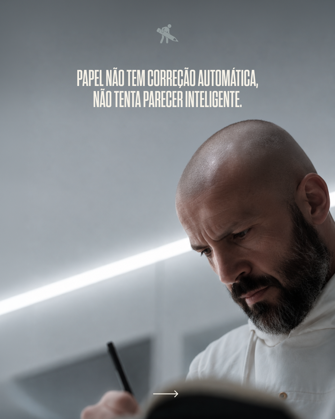 A man with a bald head and beard, focused while writing, with a gray background and white lighting. Text in Portuguese stating 'Paper does not have automatic correction, does not try to look smart'.